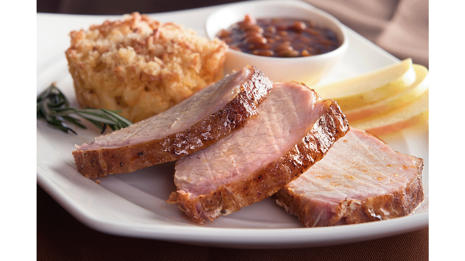 Plate with roasted pork loin, apple slices, baked beans and mac casserole