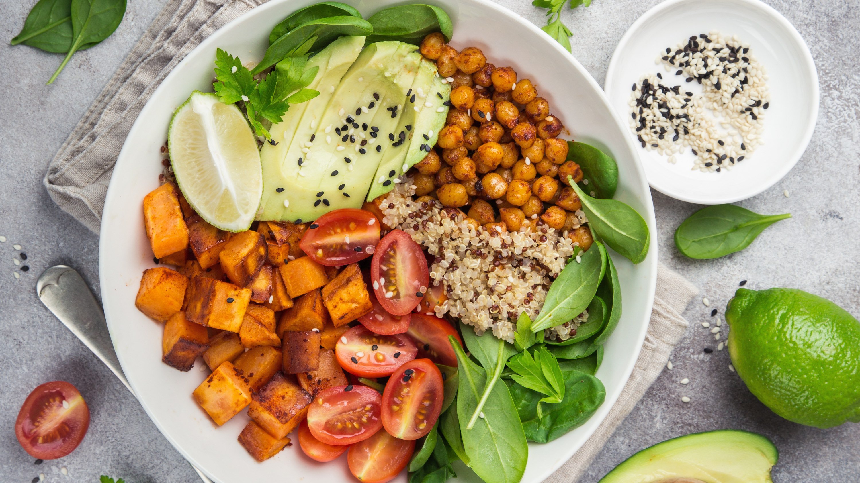 A rice bowl with avocado, spinach, cherry tomatoes, sweet potatoes and lime