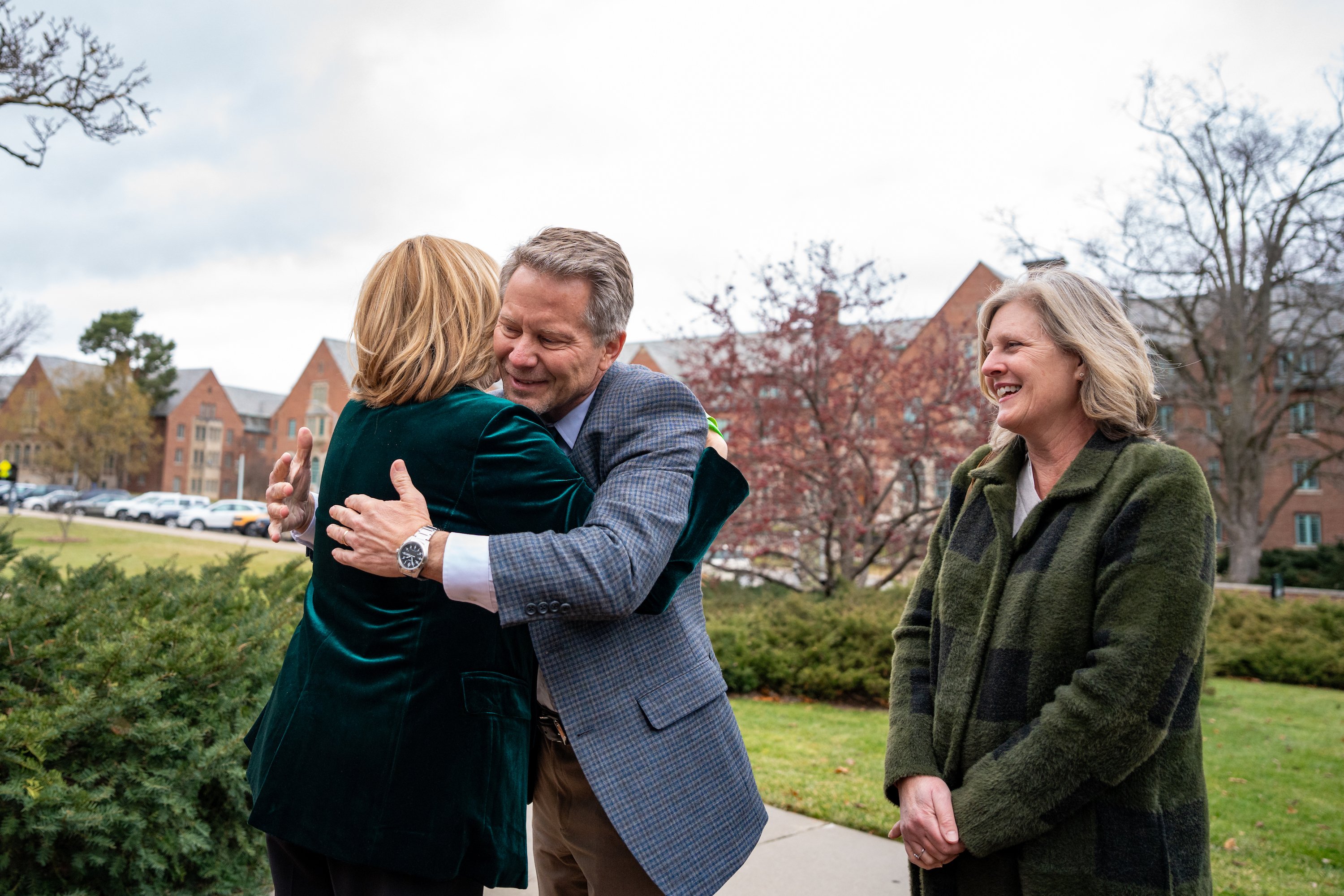 President-elect Kevin Guskiewicz greets interim president Teresa K. Woodruff with a hug, while Guskiewicz's wife Amy watches.