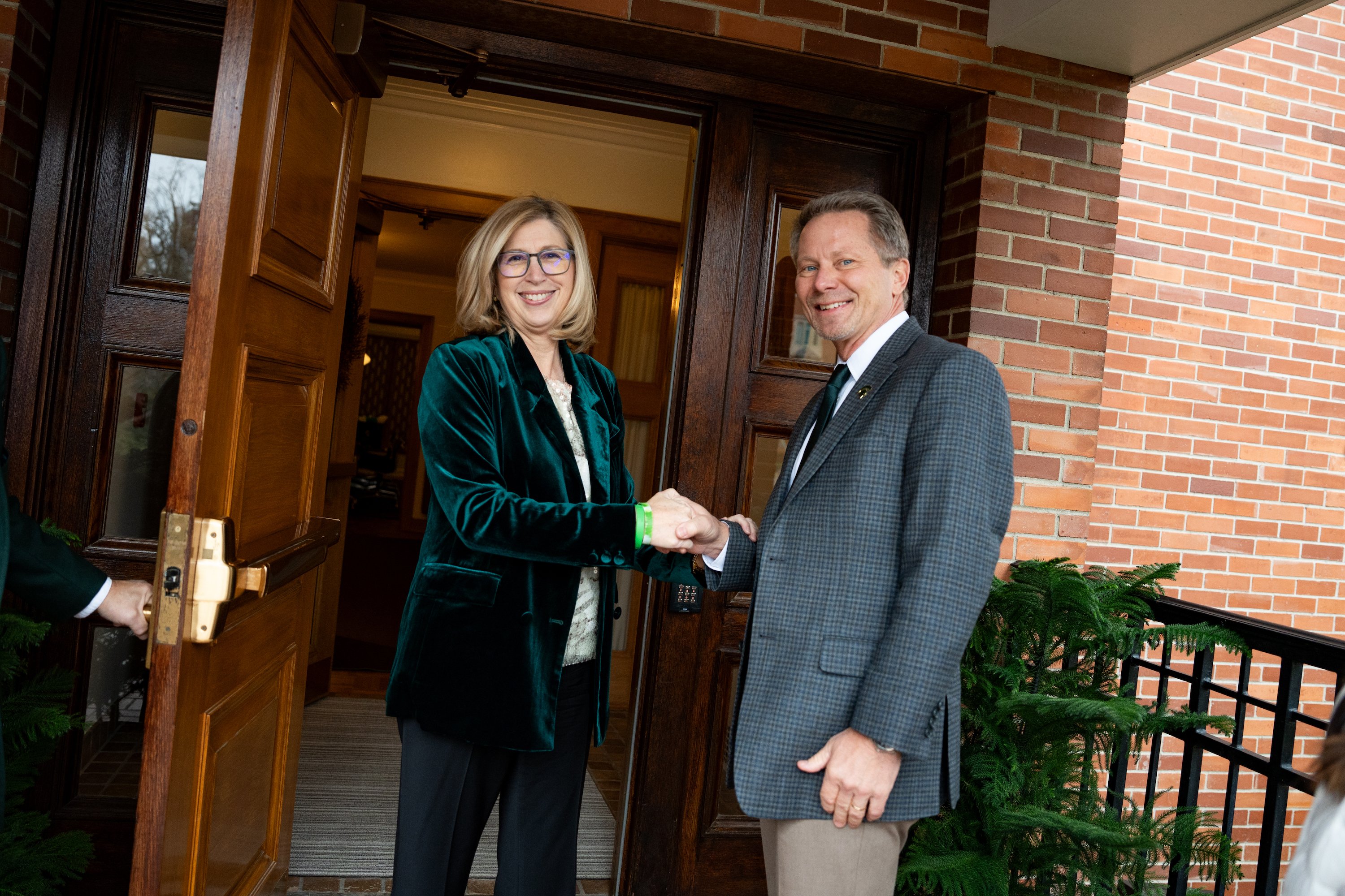 Interim president Teresa K. Woodruff and president-elect Kevin Guskiewicz shake hands in front of Cowles House.
