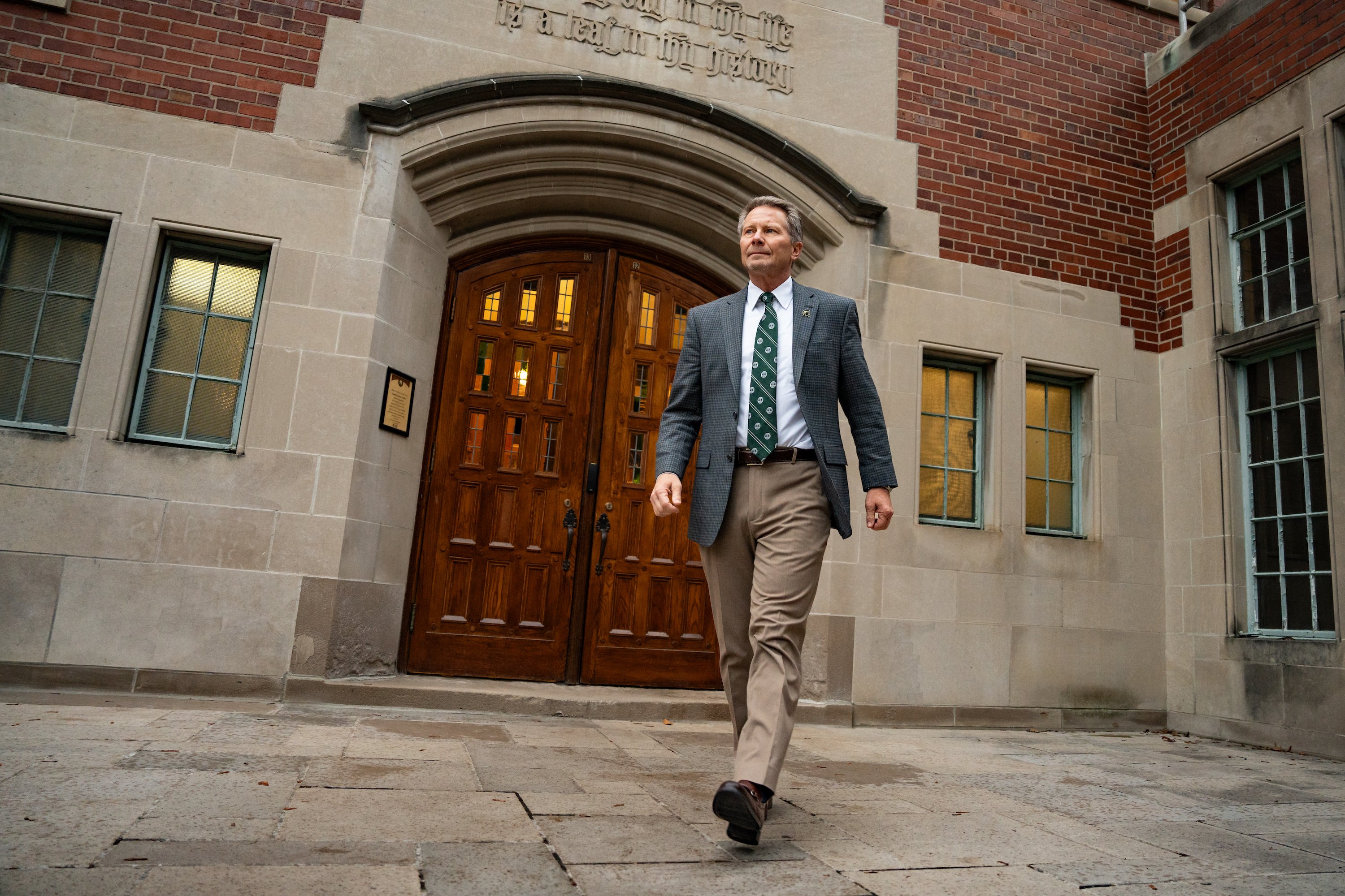 President-elect Kevin Guskiewicz walks in front of a building.