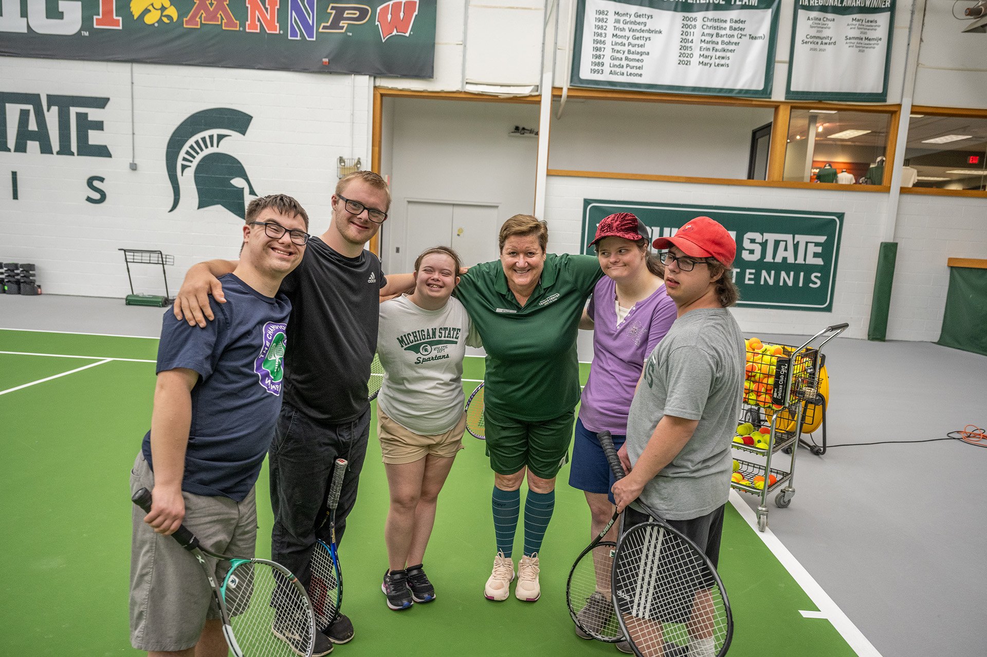 participants stand in a group photo on the court with arms over each others shoulders with the coach in the middle