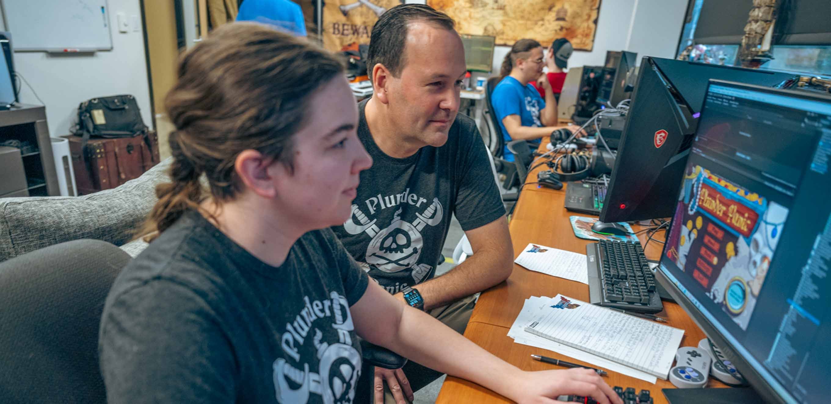 Brian Winn looks over the shoulder of woman employee of Will Winn games as she works on ?Plunder Panic? updates on a computer.