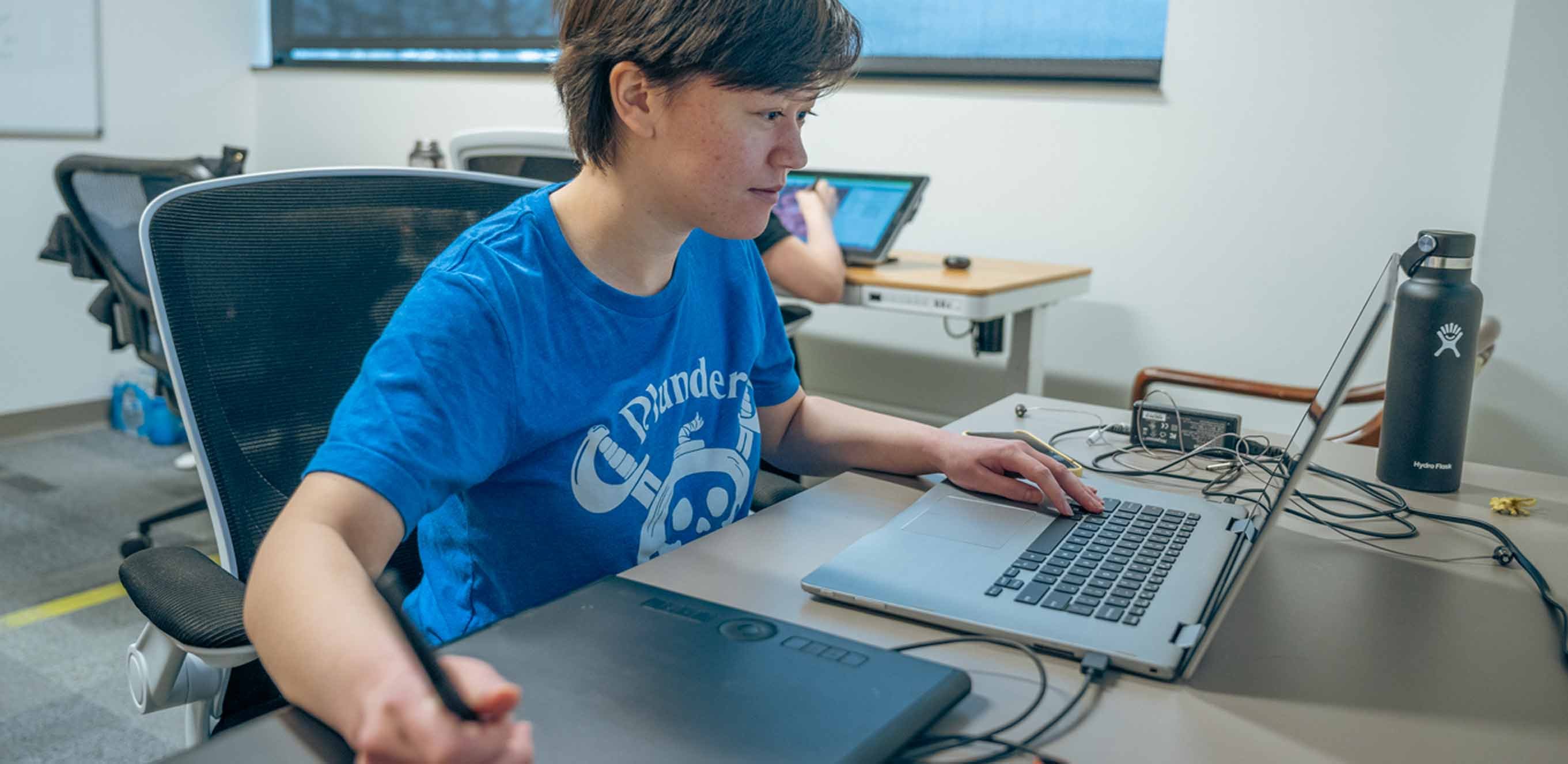 Tatum Cho looks at a computer while drawing on a digital tablet.