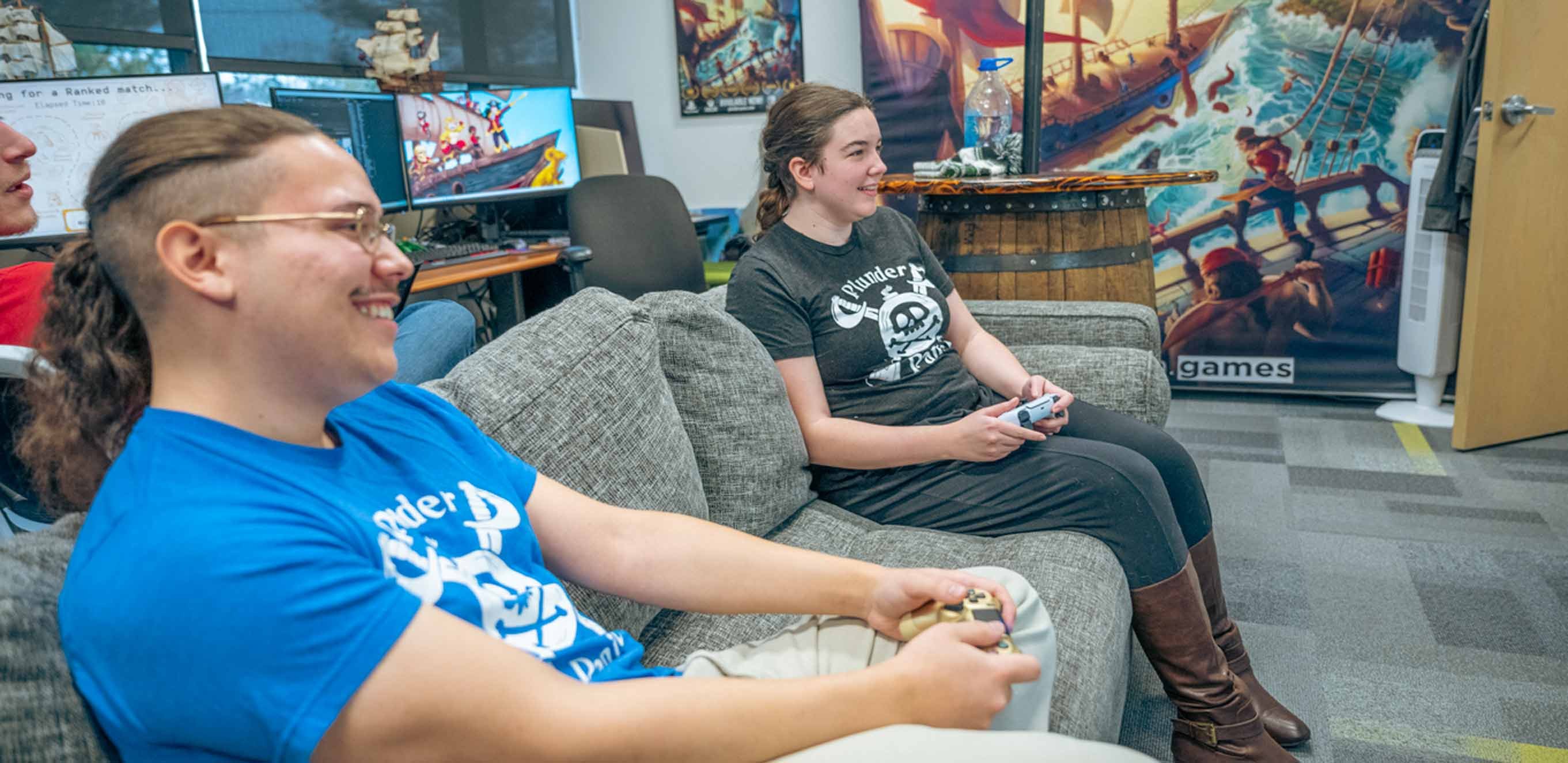 A man and woman play a video game on a couch while wearing ?Plunder Panic? t-shirts.