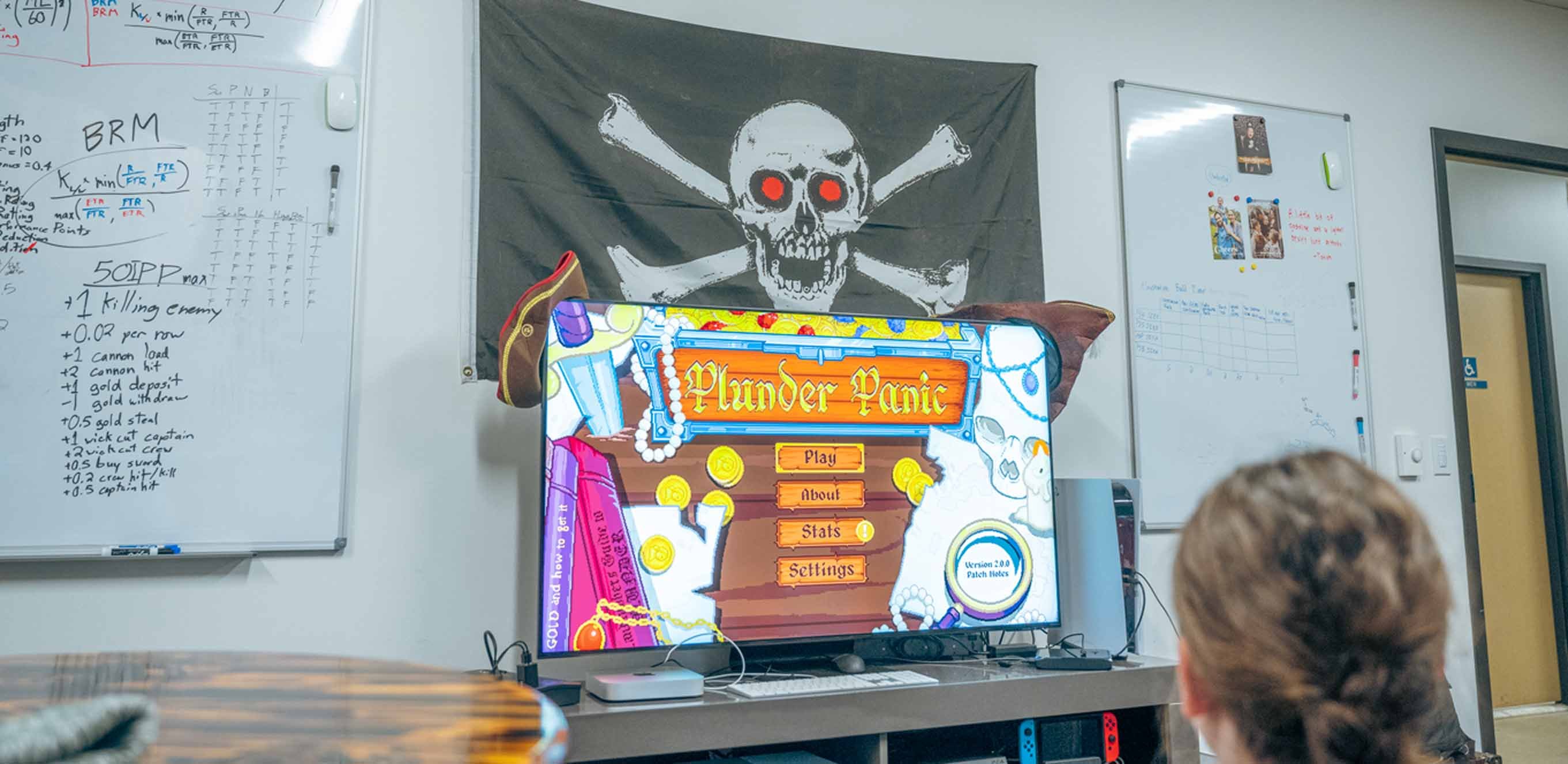 A TV displaying the ?Plunder Panic? launch screen. A pirate flag is on the wall above the TV, and there are whiteboards on the walls to the left and right of the TV.