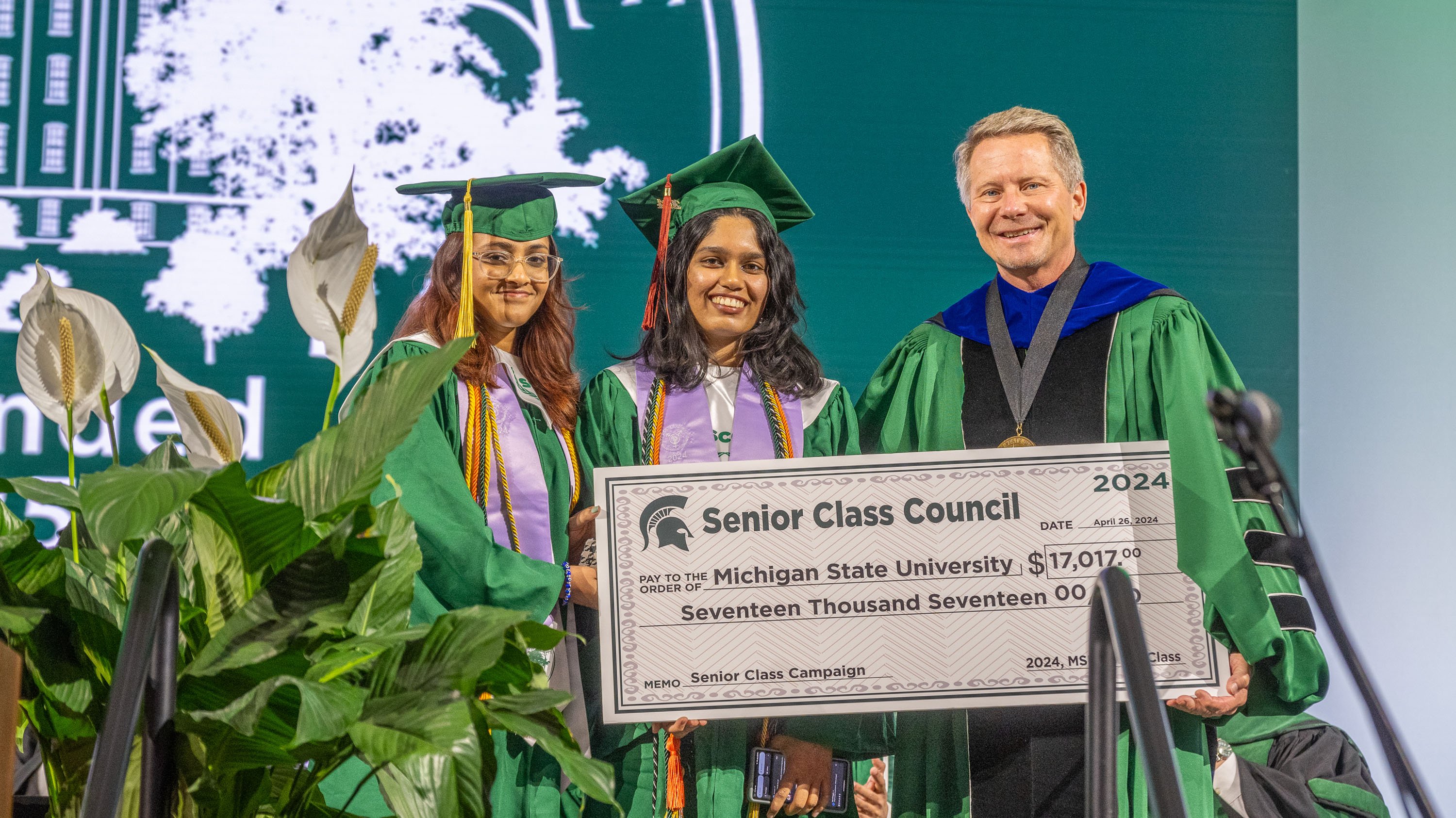 Shrishti Jalan (left) and Shruti Elango holding giant check with Kevin Guskiewicz at convocation