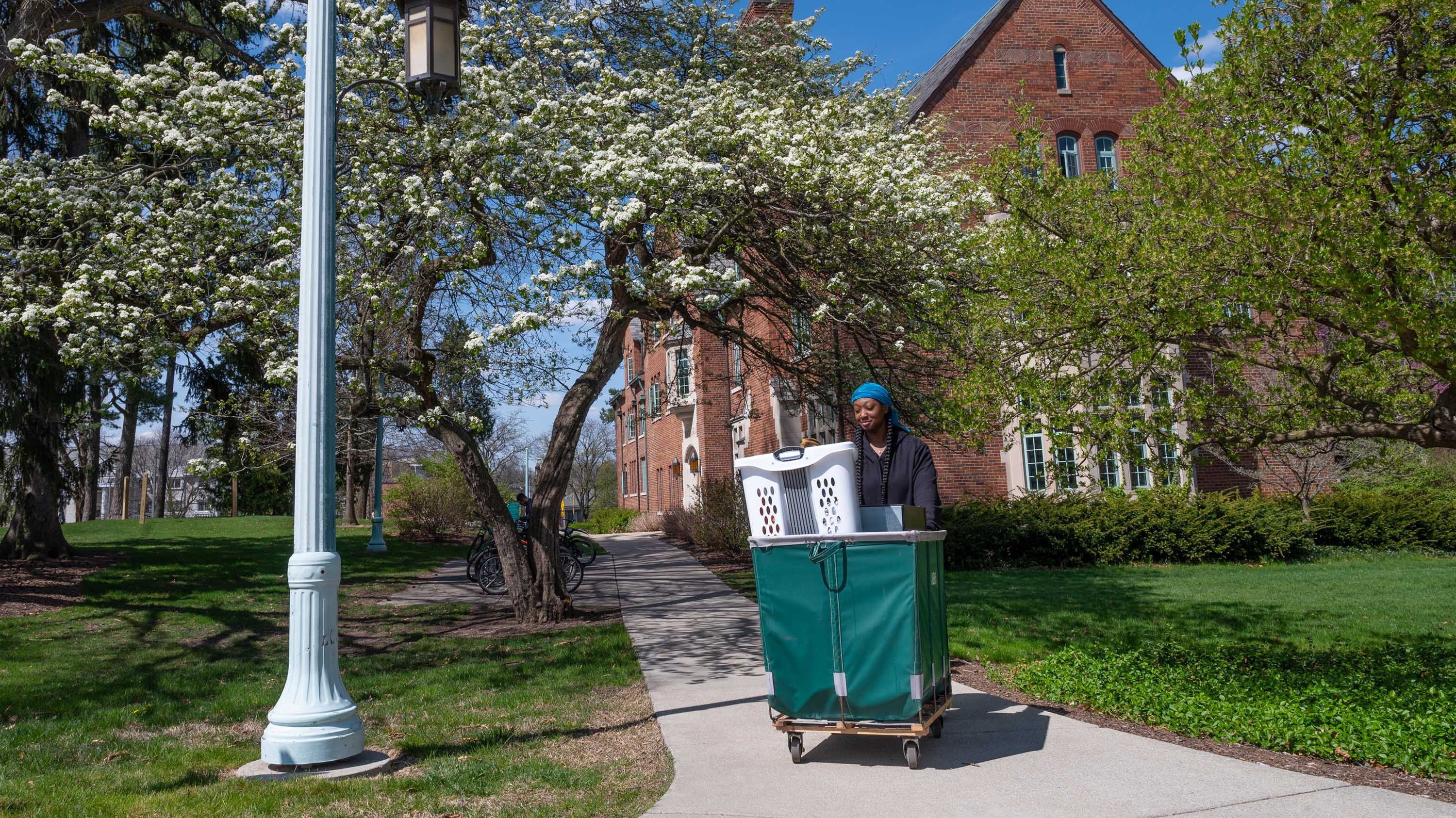 Student moving belongings out of residence hall in green laundry cart