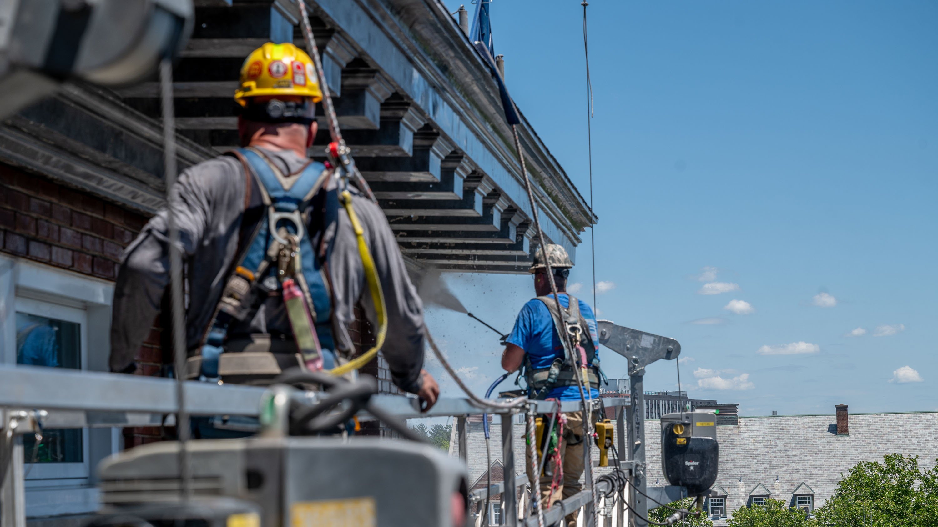 Two people pressure-washing dentil molding on Agriculture Hall