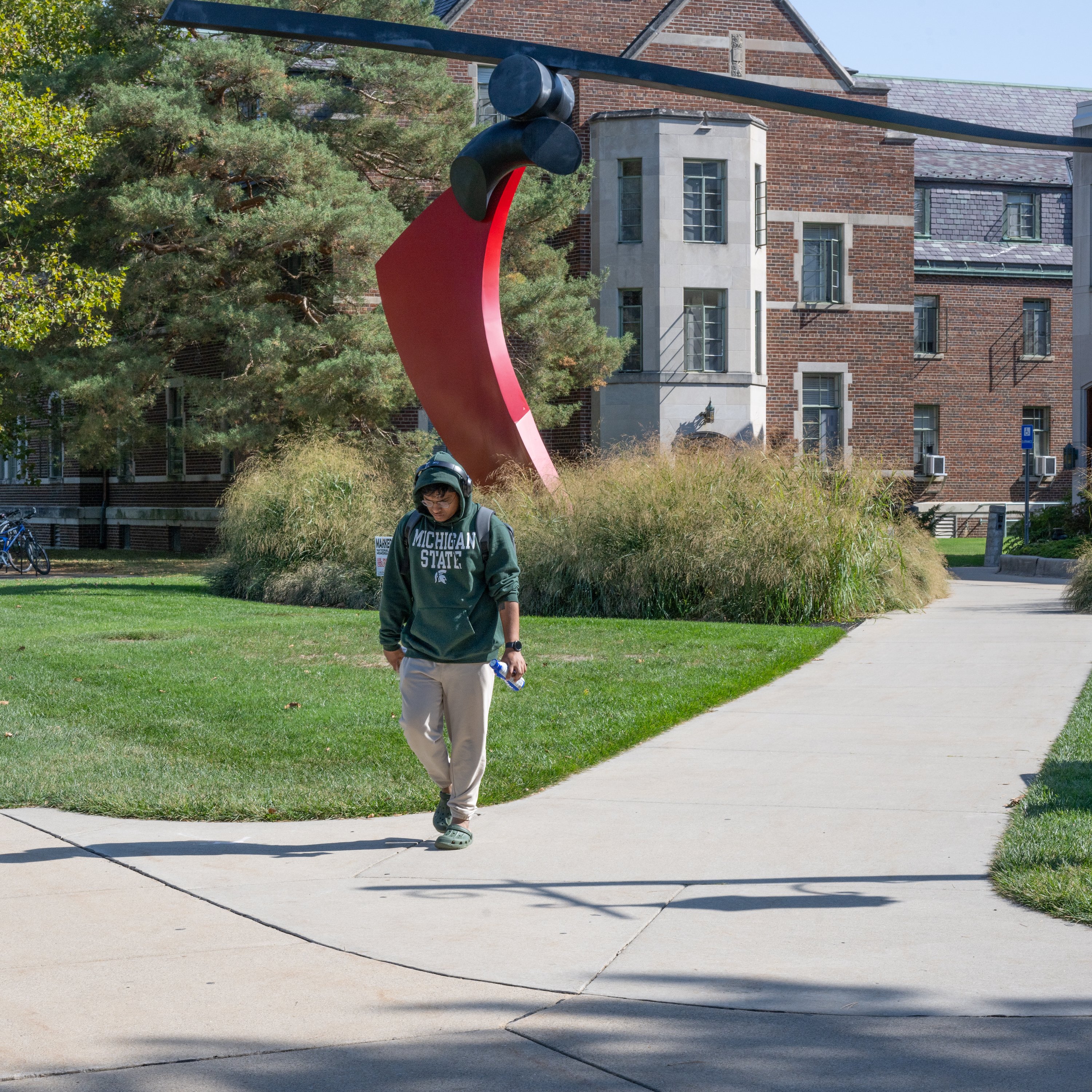 A student walking in front of a red statue with a brick building in the background.