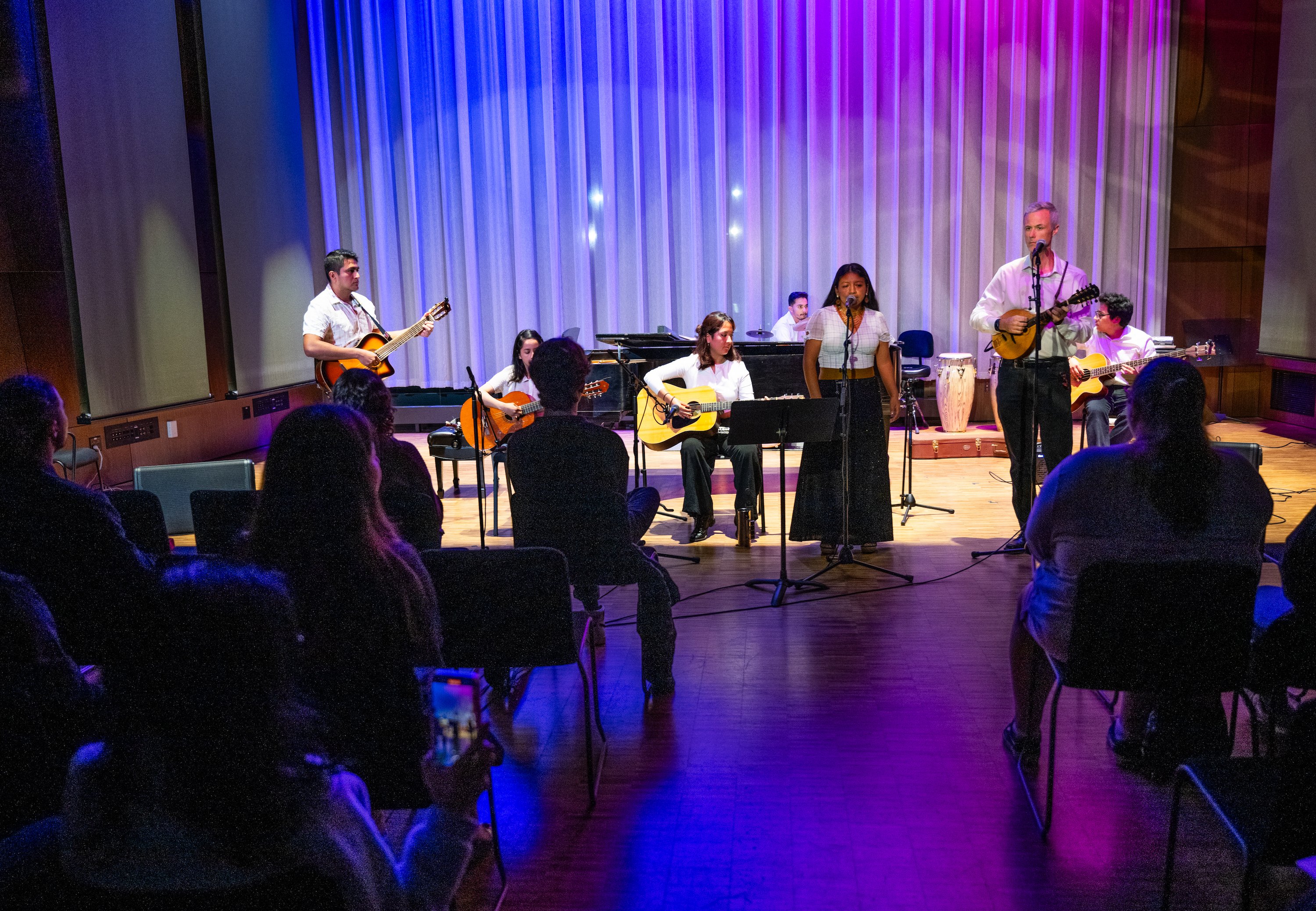 Musicians play musical instruments on a stage with blue an purple uplighting.