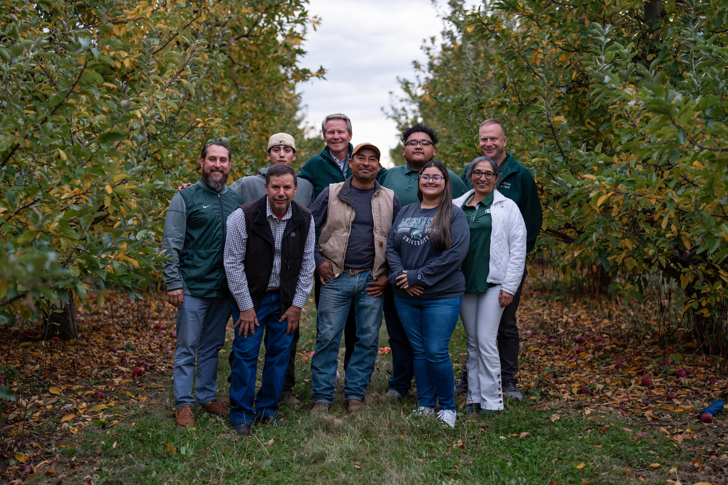 A group of people pose within an apple orchard.
