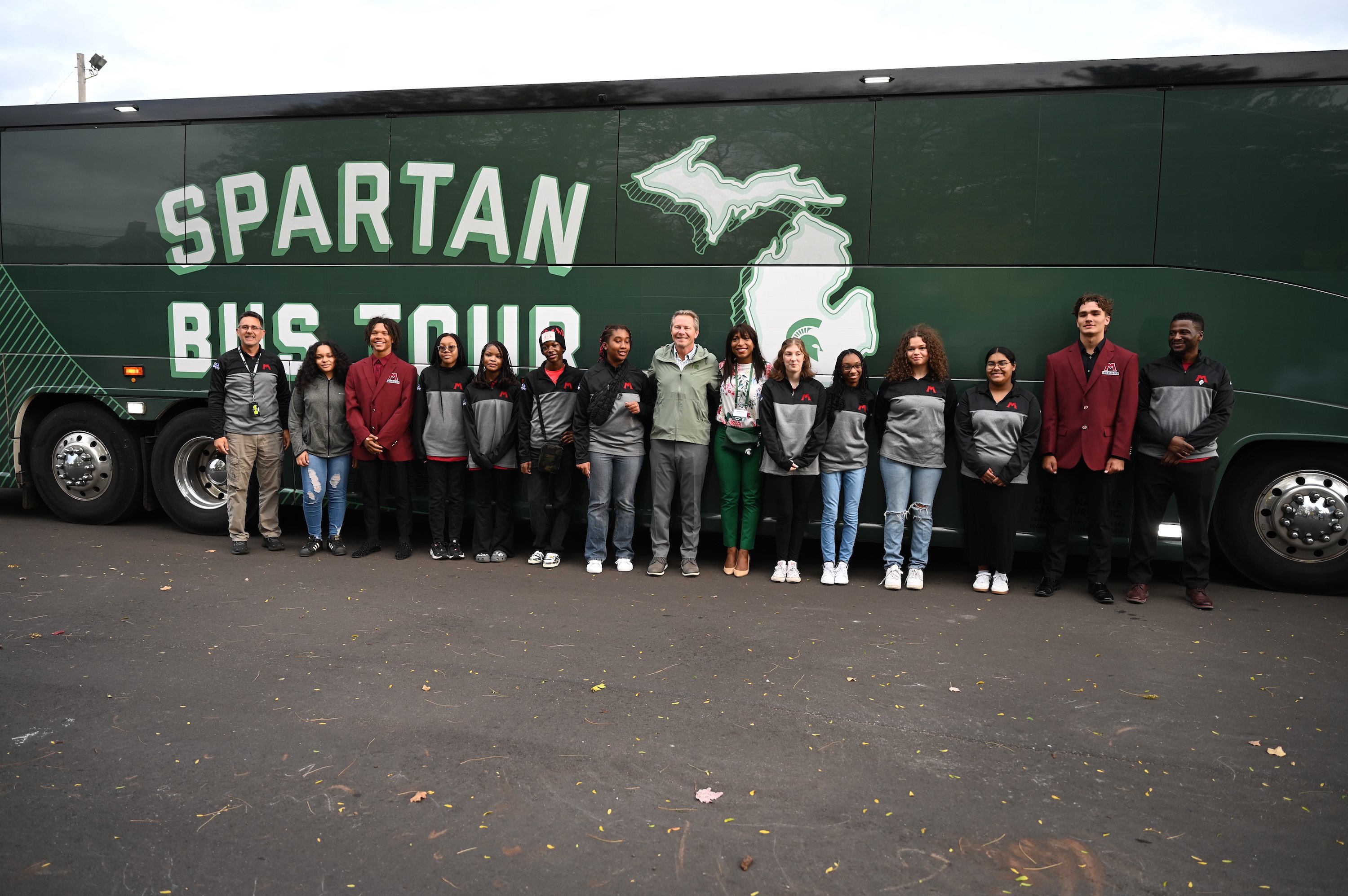 People pose in front of the Spartan Bus Tour bus.