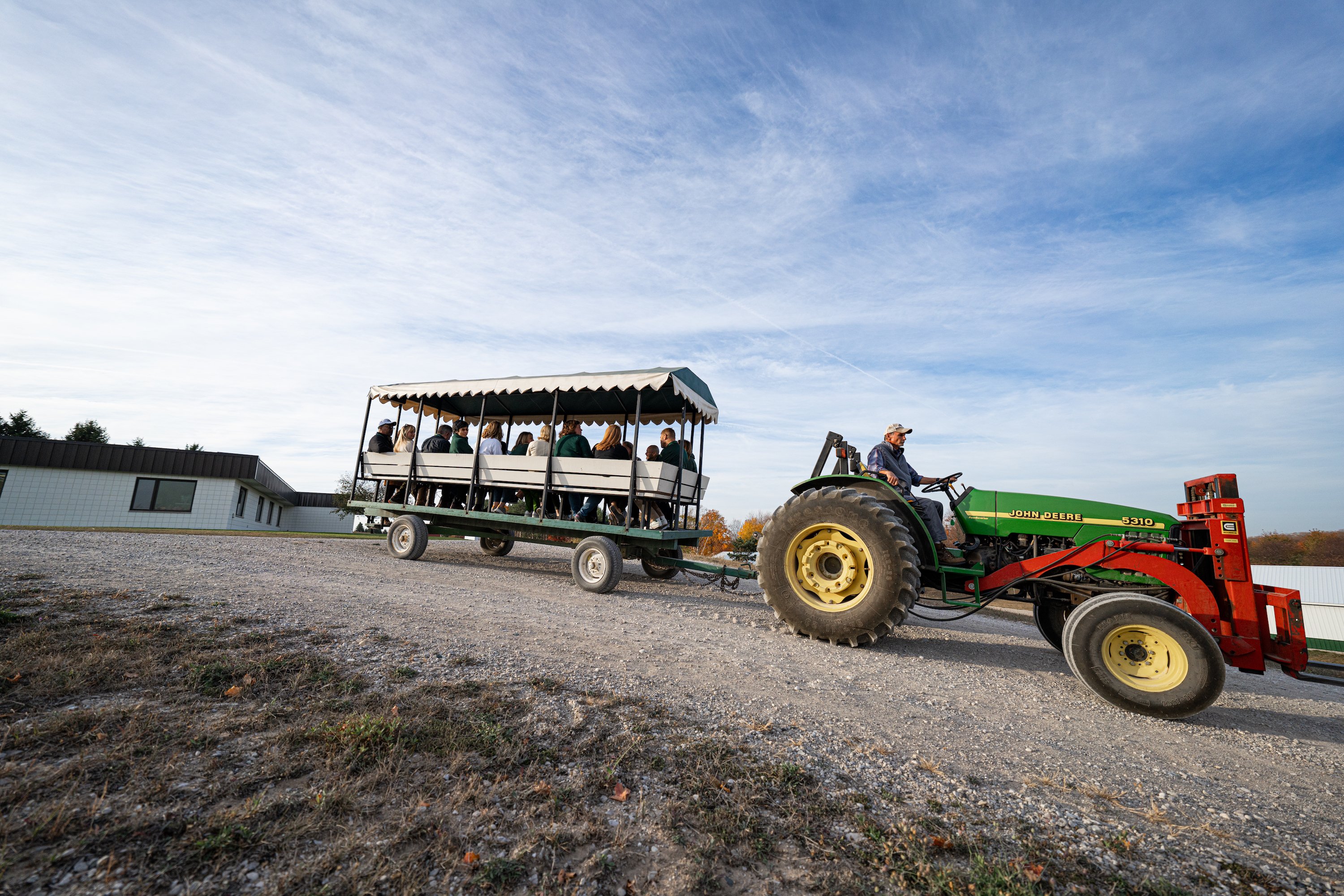 A tractor pulls a wagon filled with people across a dirt road.