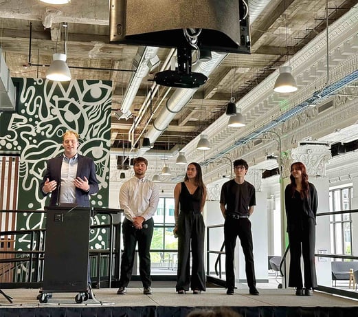 An individual speaking at a podium while four other people look on.