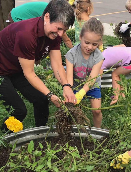 An adult helps a child with a plant outside.