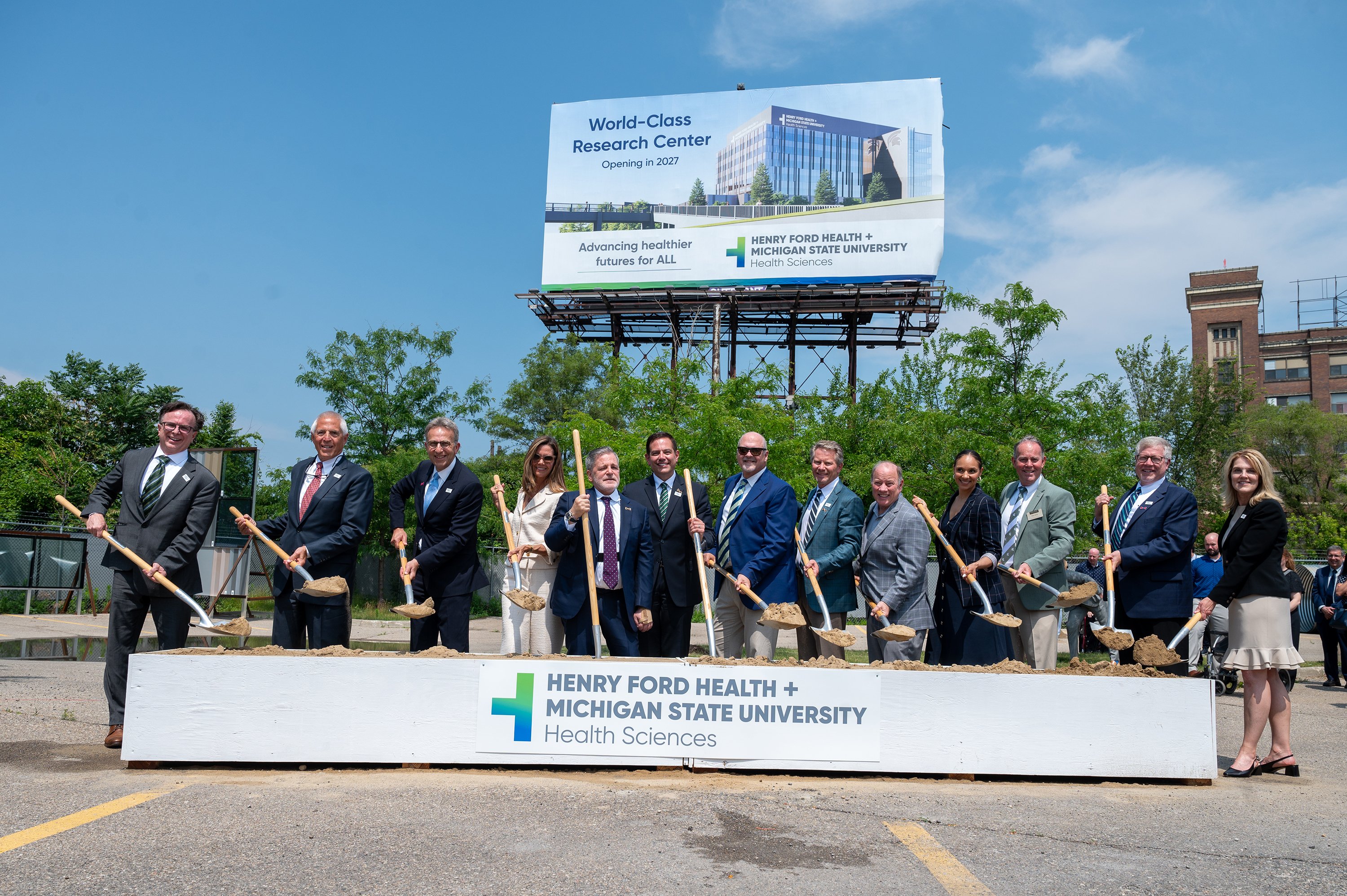 Participants, including the Michigan State University mascot, shovel dirt at the groundbreaking ceremony for the new Henry Ford Health + Michigan State University Health Sciences.