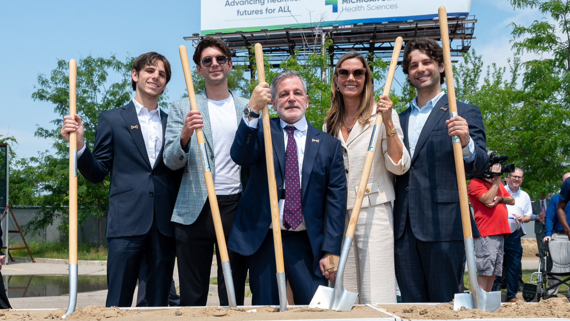 Five people hold shovels during the groundbreaking ceremony, ready to participate in the ceremonial first dig.