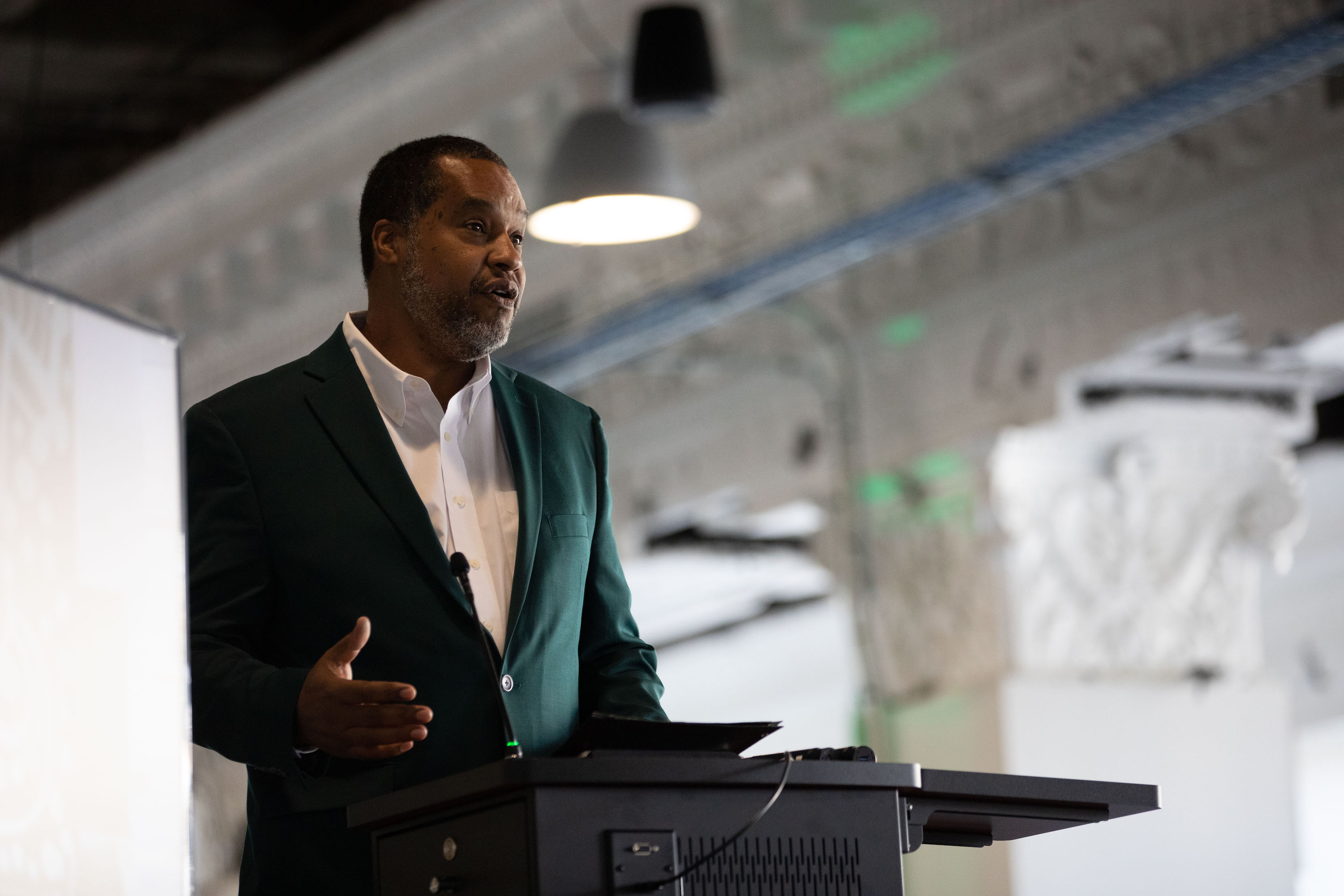 Dave Weatherspoon speaking at a lectern wearing a green jacket.