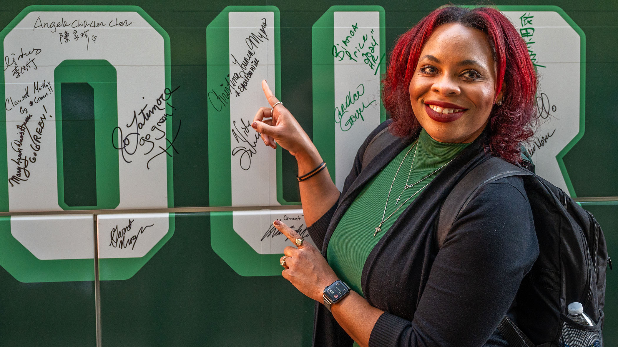 A person points to their signature in a white letter “U” on a green bus.