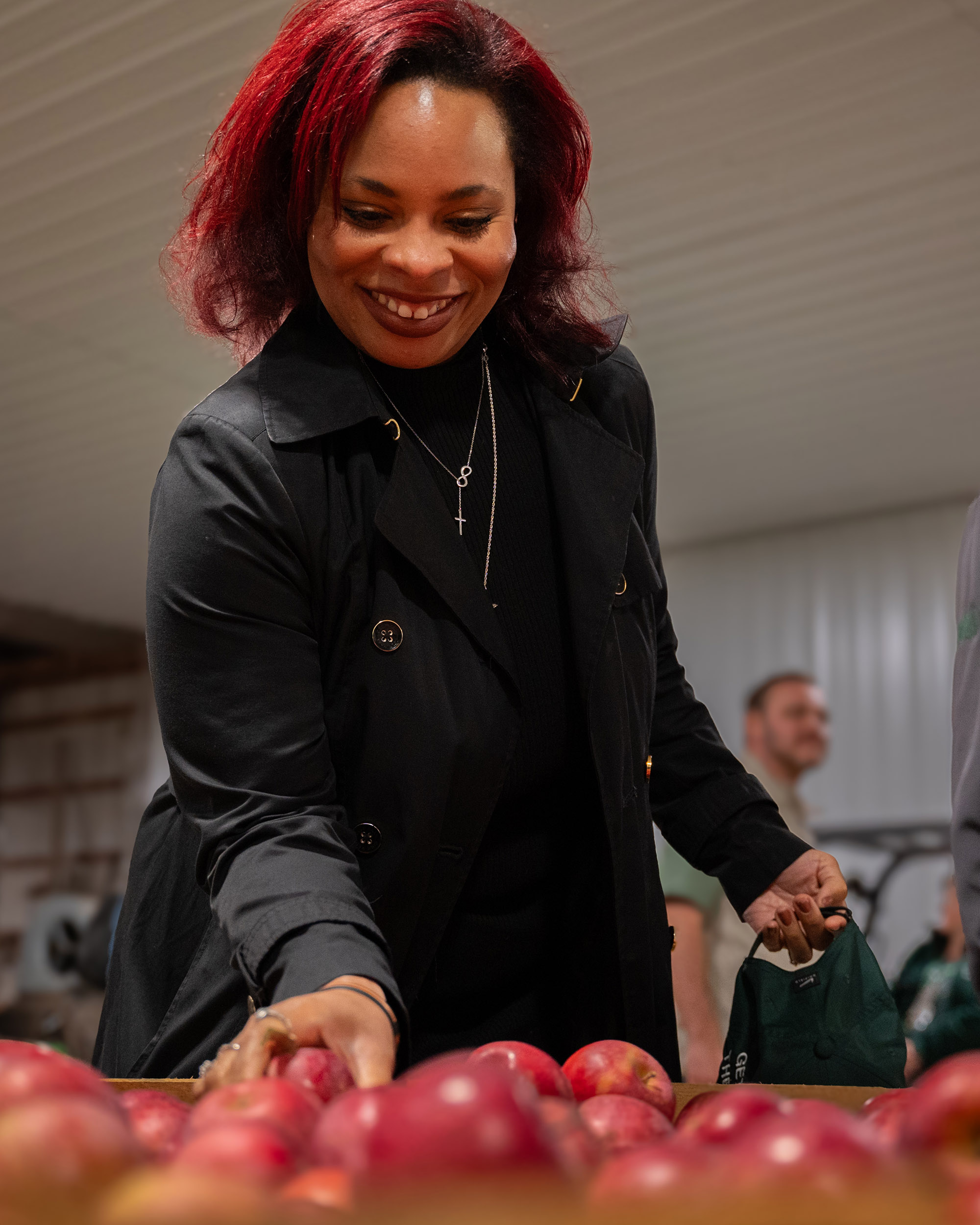 A person smiles while picking an apple out of a crate full of apples.