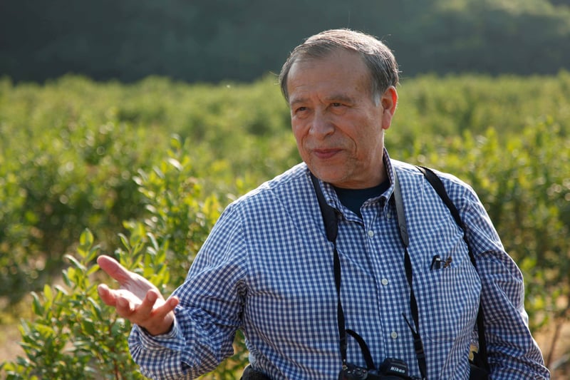 David Mota-Sanchez is gesturing with his right hand outstretched while speaking and standing among rows of blueberry bushes