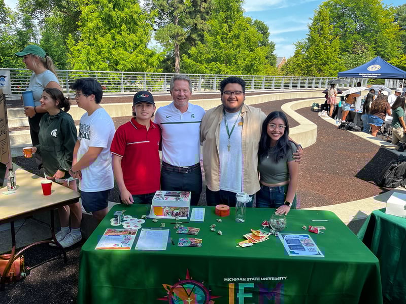 students pose with president Guskiewicz at a tabling event