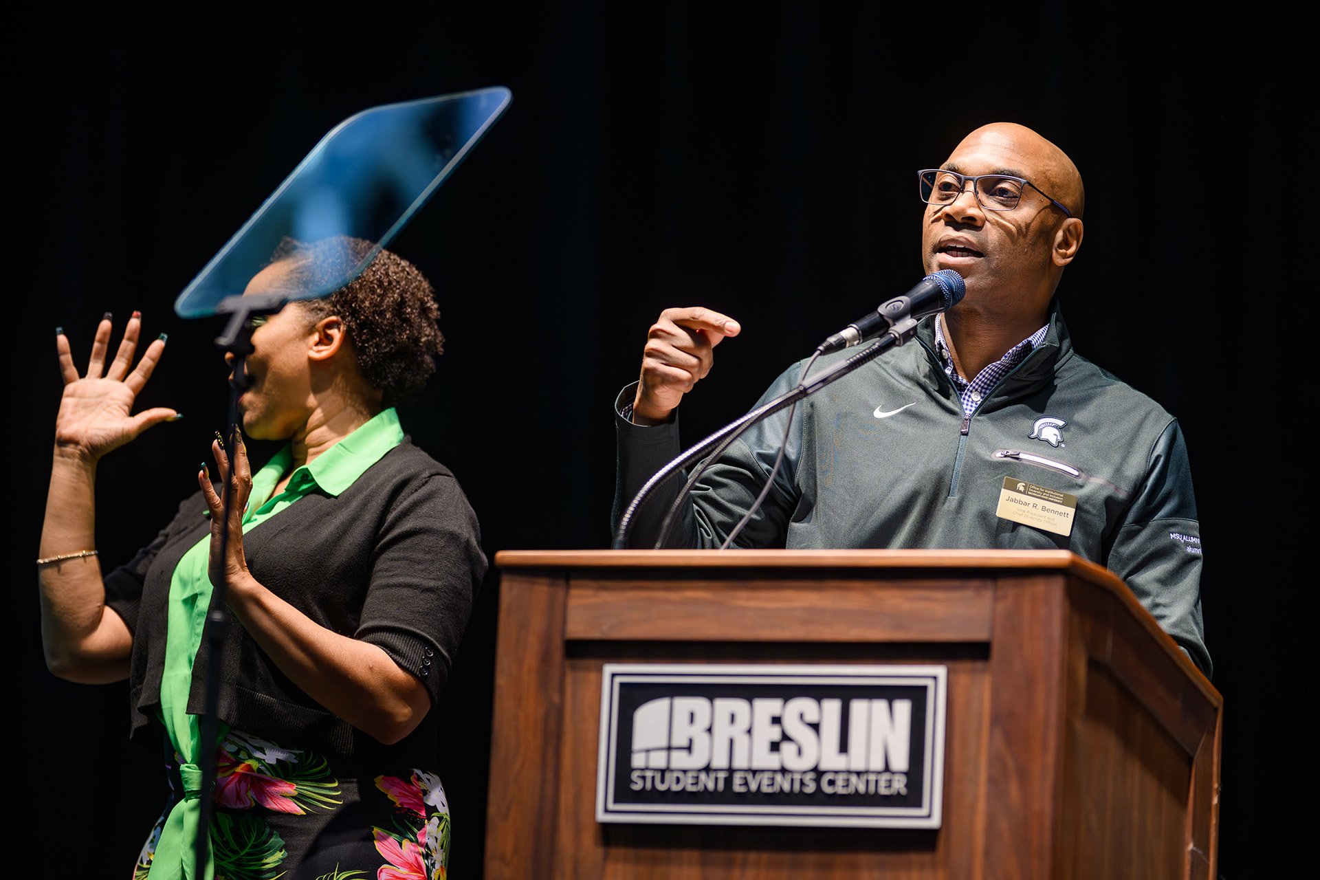 Jabbar Bennett speaks at the lectern with an interpreter making sign gestures next to him