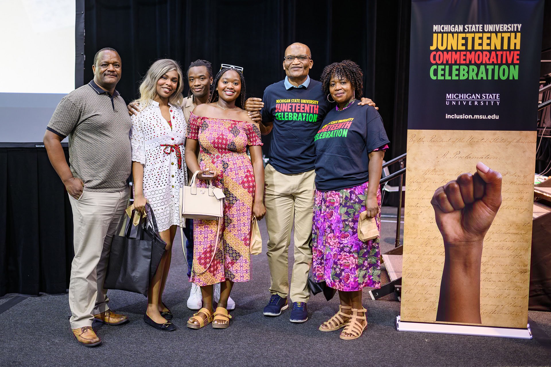 Participants take a group photo with a Juneteenth banner next to the stage