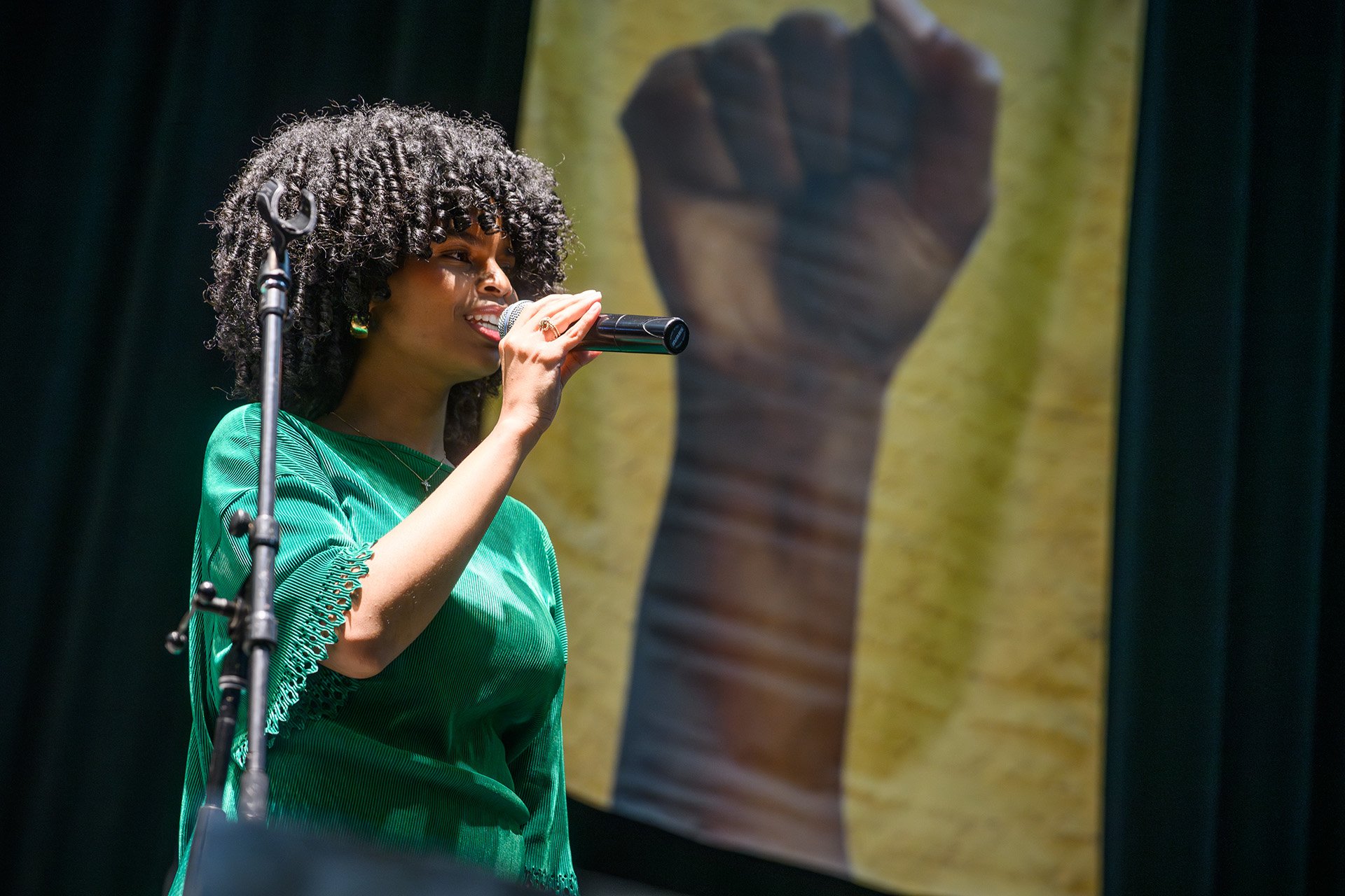Phoenix Miranda sings at the mic with the Juneteenth banner in the background