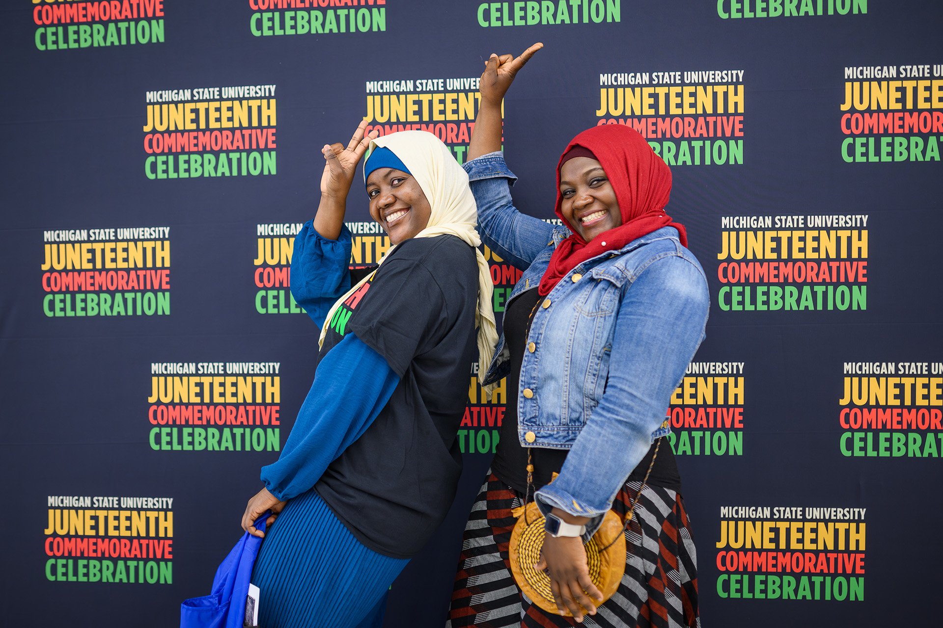 Juneteenth attendees in scarves strike a pose in front of the Juneteenth step-and-repeat backdrop