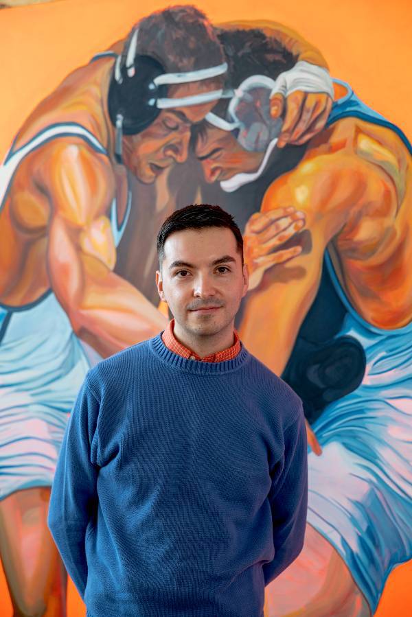 MFA candidate Gustavo Uriel Ayala standing in front of his painting, titled “Between the Legs,” which is included in the 2024 Masters of Fine Arts Exhibition.