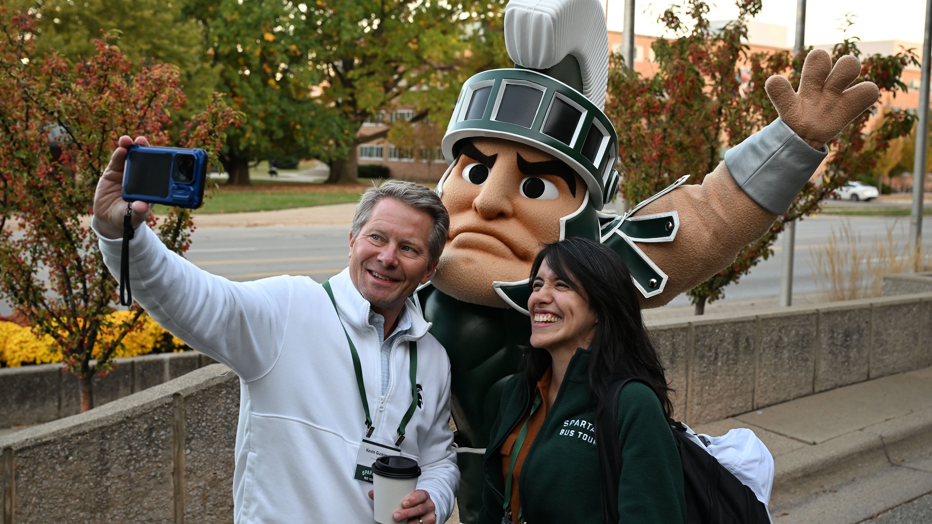 Two people pose for a selfie with Sparty.
