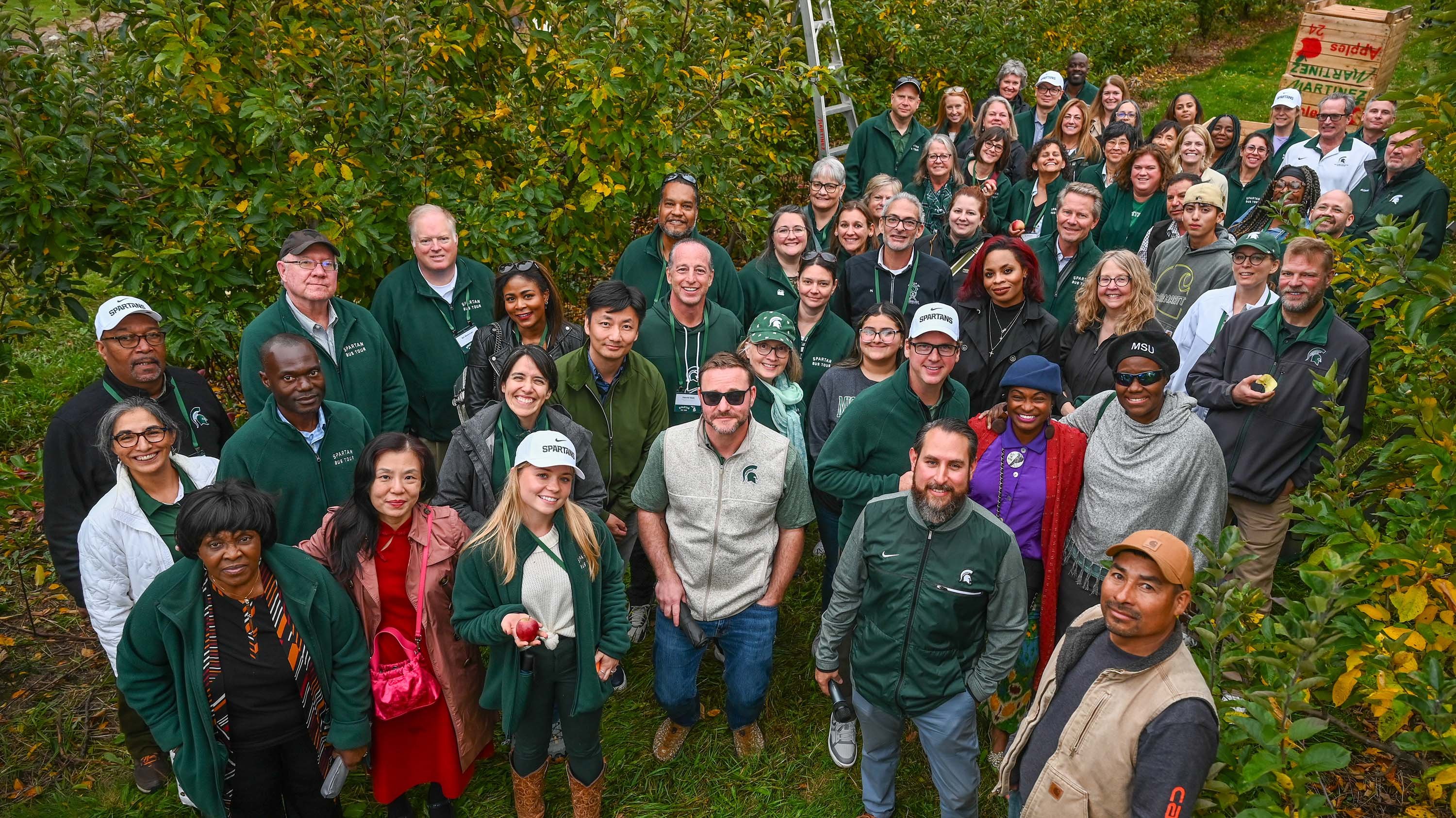 A group of people pose for a photo in an apple orchard. 
