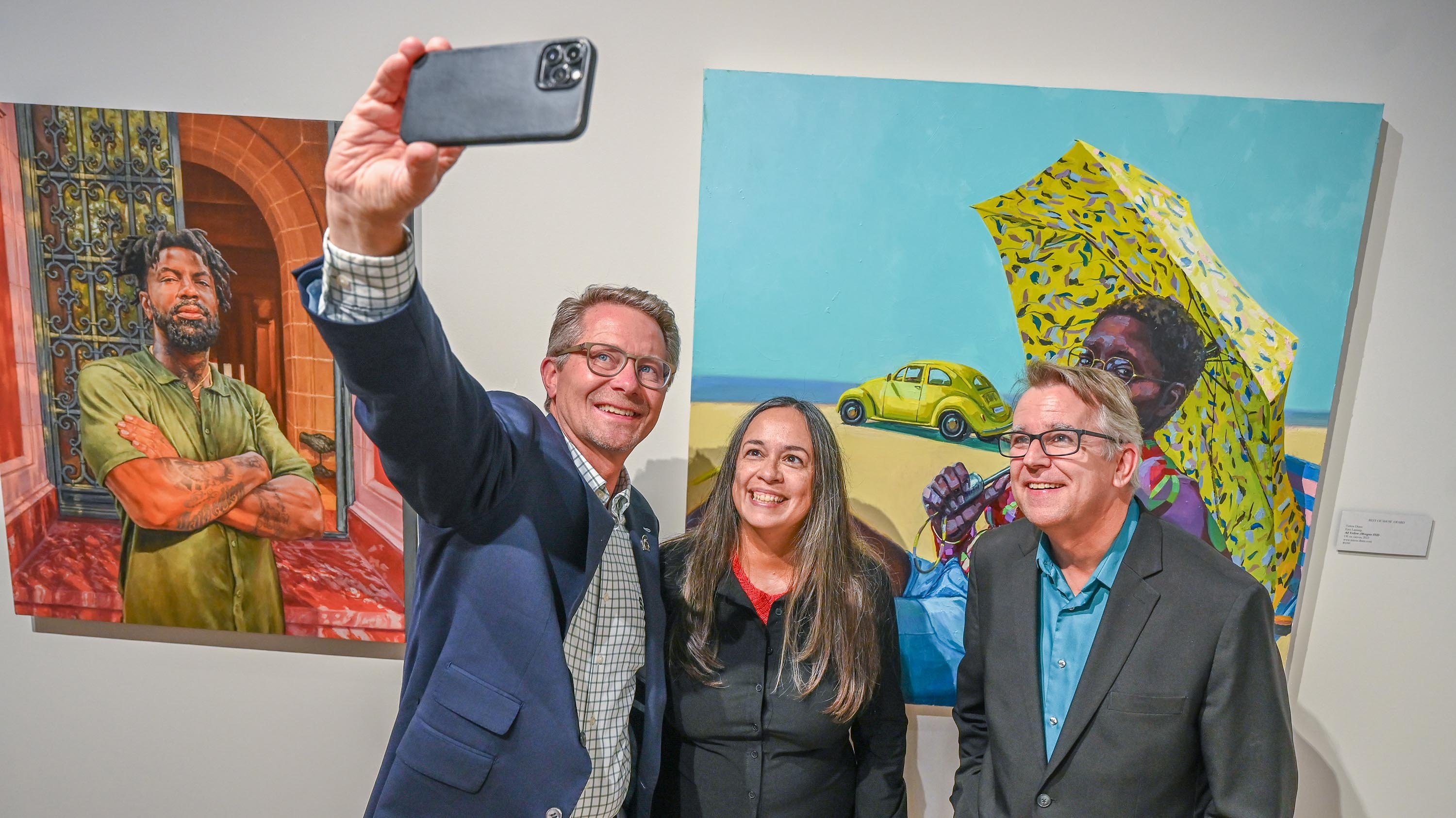 Three people pose for a selfie in front of a colorful painting.