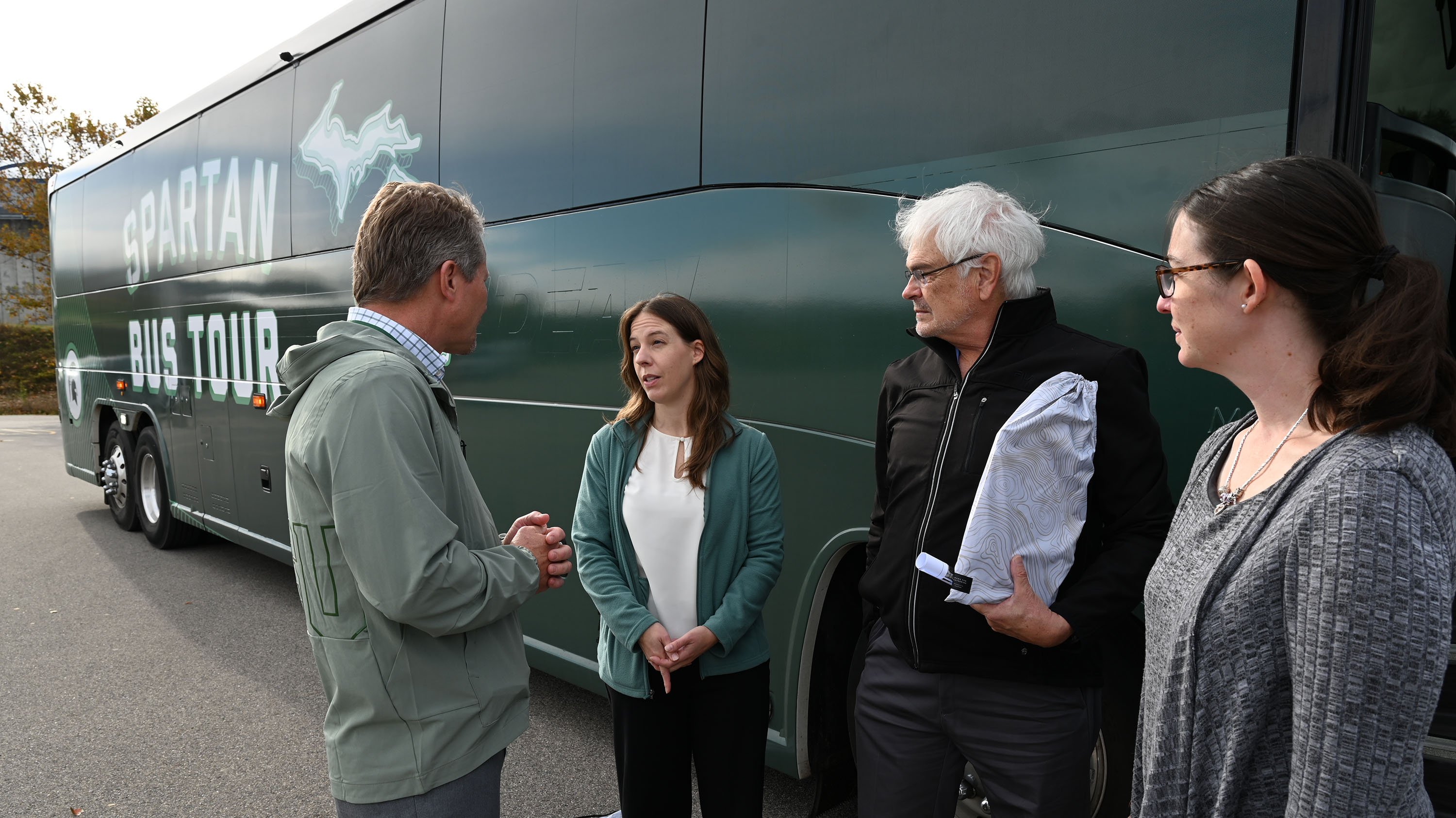 Four people talking outside of a green bus.