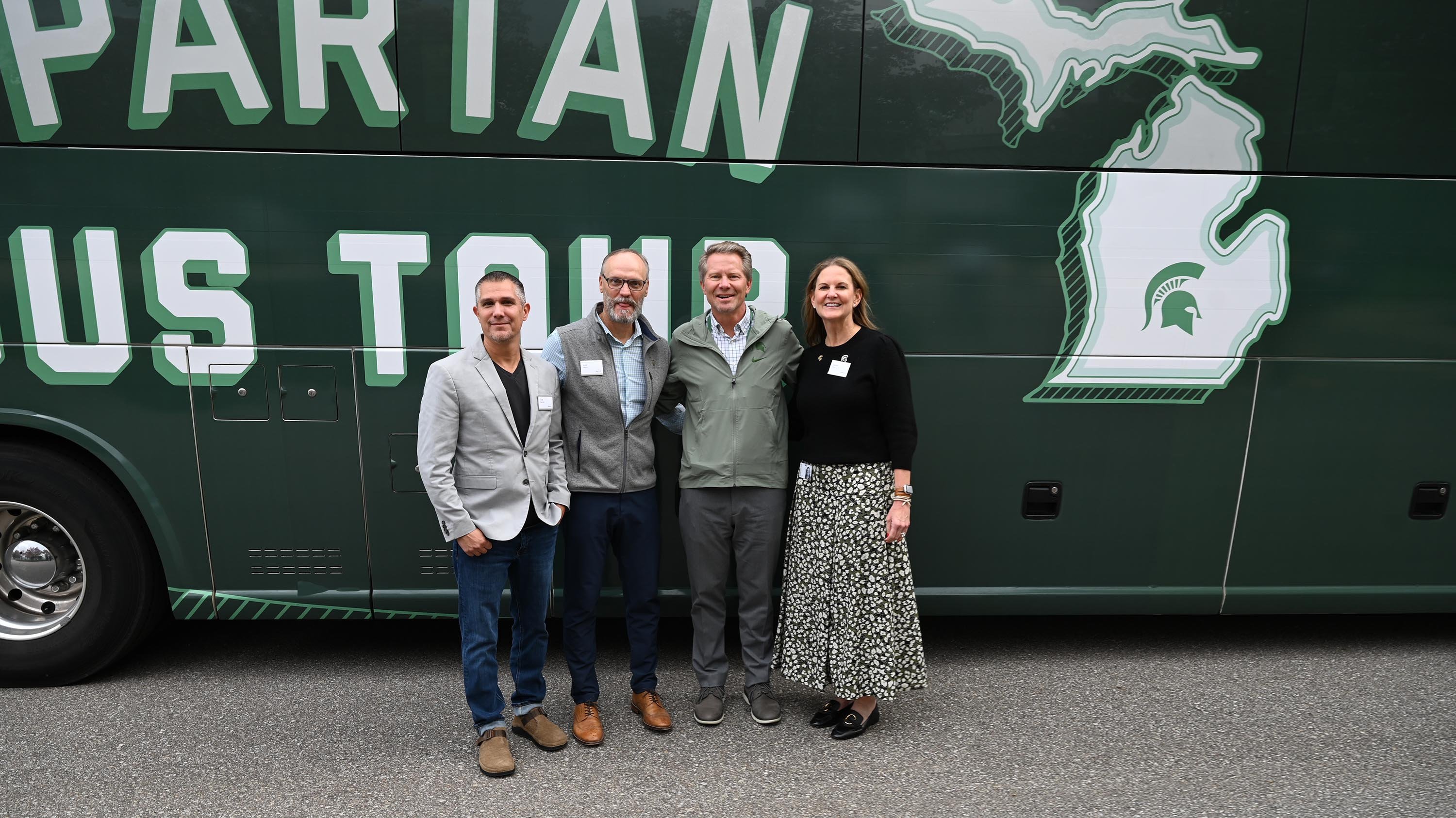 Three people posing in front of a green bus.