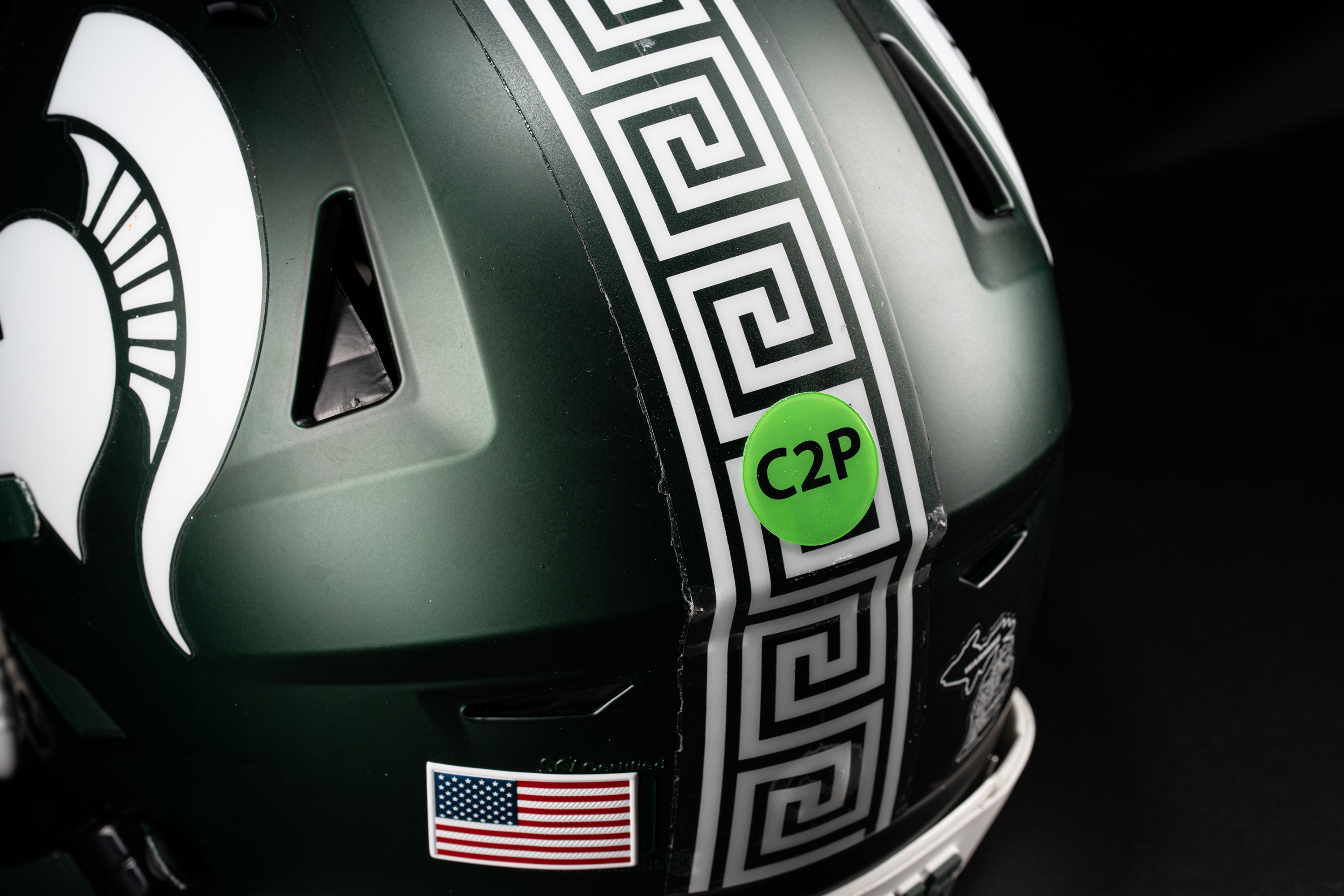 The back of a green football helmet with a white stripe down the middle and a neon green circular sticker that says “C2P”