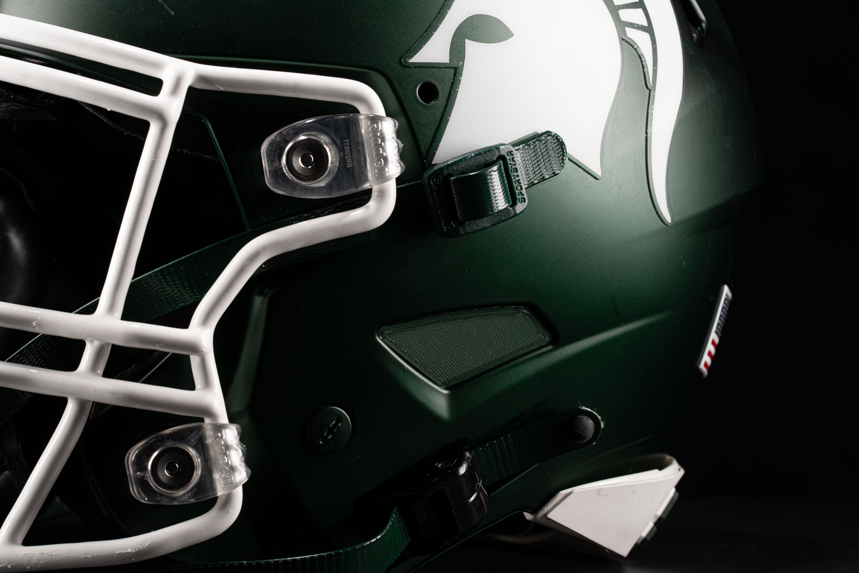 Close up of an insert on a football helmet earhole. The helmet is green with a white Spartan helmet logo.