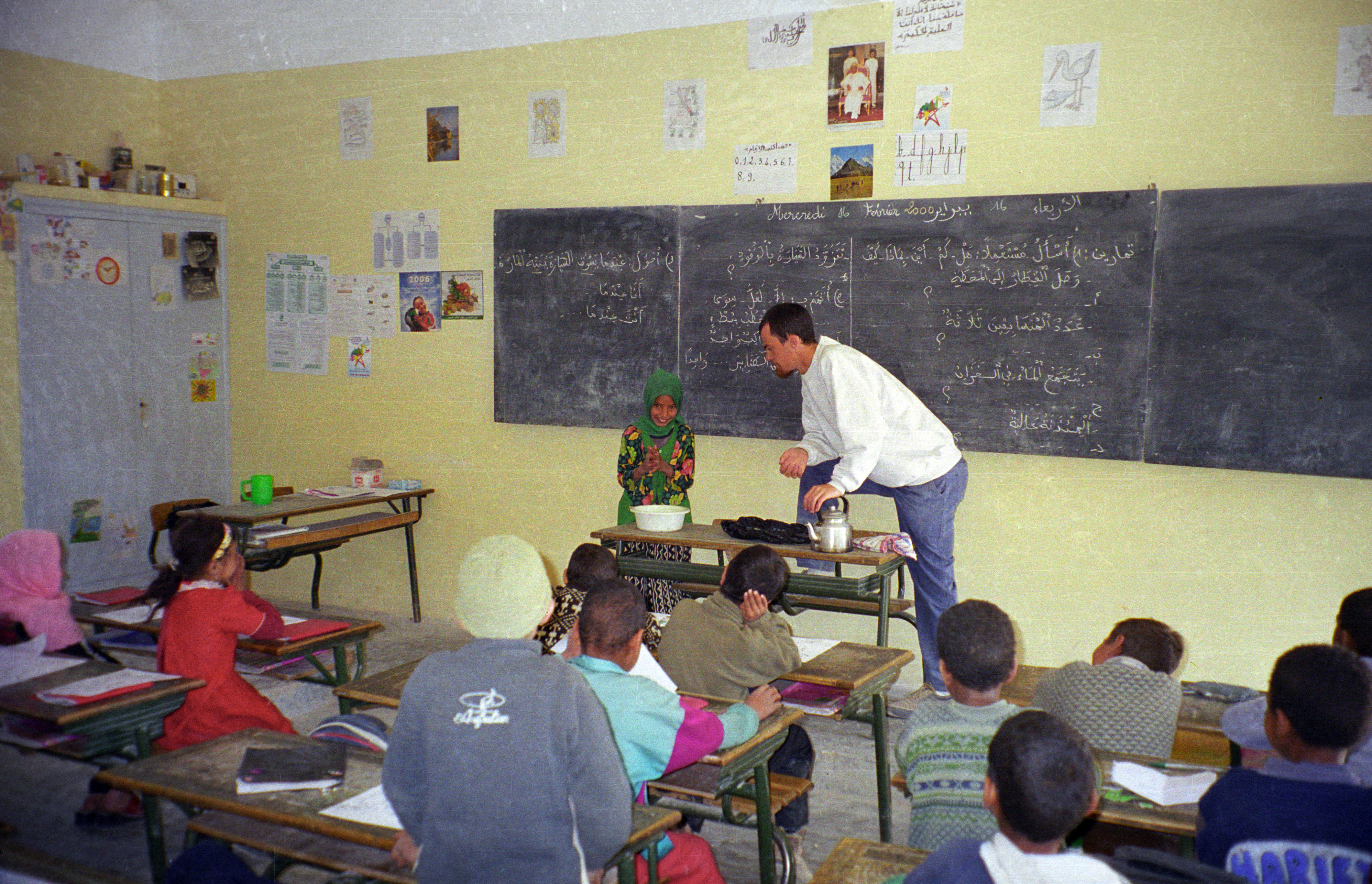 A teacher looks on as a young girl washes her hands.