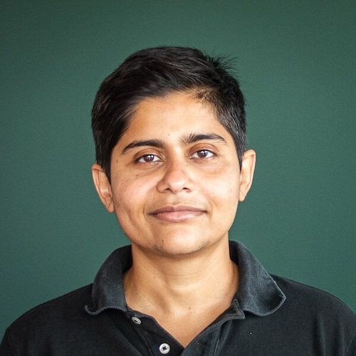 Portrait of Megh Marathe posing in front of a green wall.
