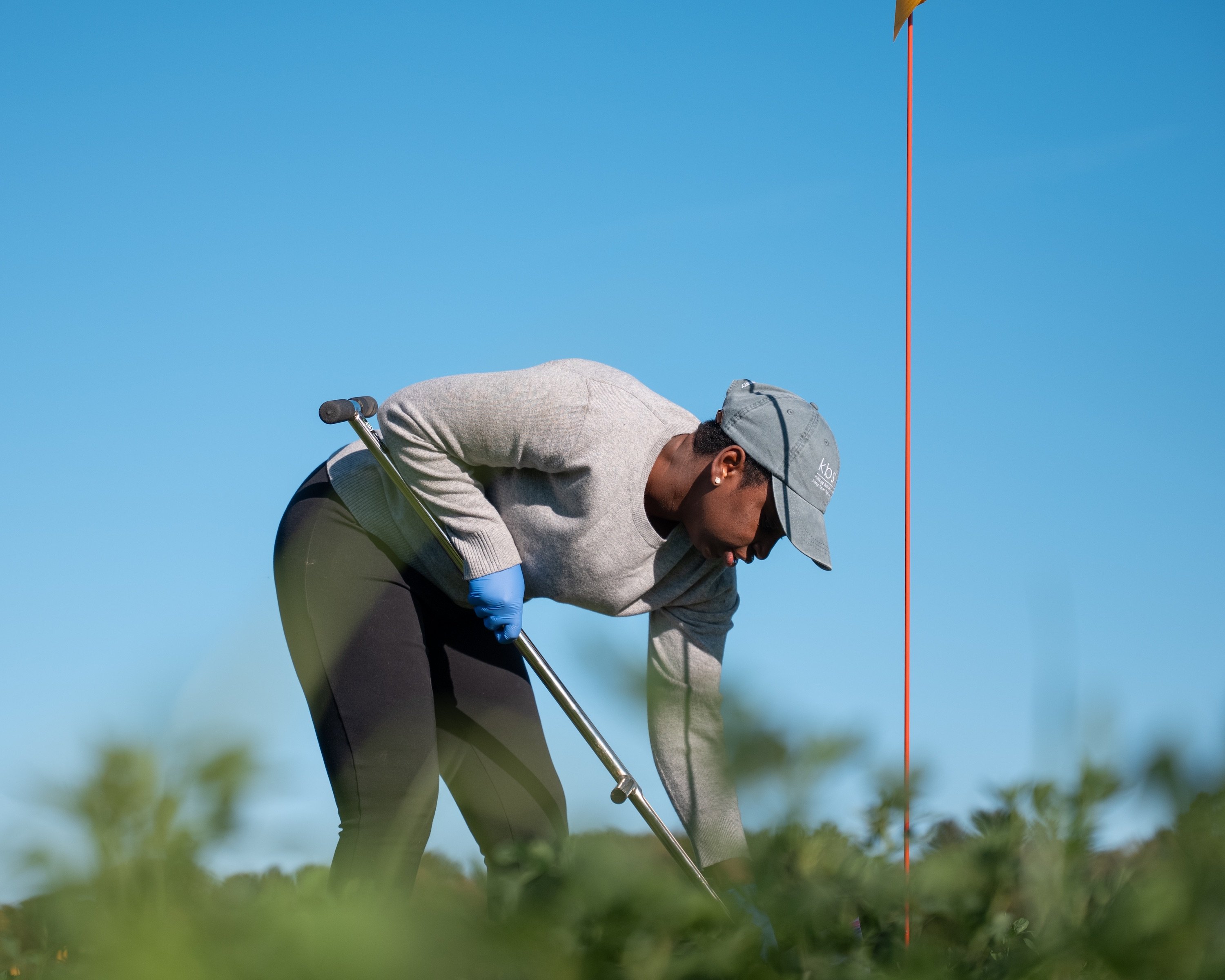 A woman wearing a hat takes a soil sample in a field