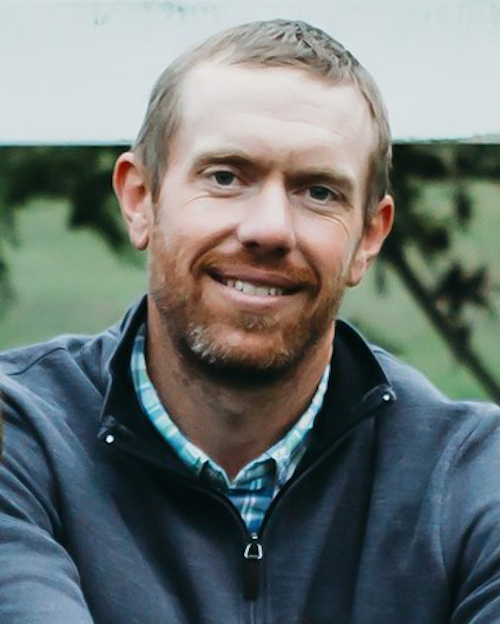 A portrait of Brook Wilke wearing a quarter-zip sweater over a blue-checkered shirt