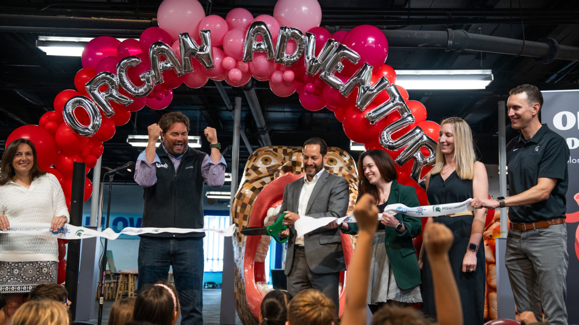  Left to right: Erik Larson, executive director of Impression 5 Science Museum, celebrates as Seth Ciabotti, executive director of MSU Health Care, cuts the ribbon for the new Organ Adventure exhibit. Also participating in the ribbon cutting (from left) are Jennifer Needham, board chair of the Impression 5 Science Center; Lindsay Gluf-Magar, marketing coordinator for MSU Health Care; Jill Moschelli, MSU Health Care Sports Medicine physician and associate professor of orthopedics in the MSU College of Human Medicine and the MSU College of Orthopedic Medicine; and Robert Root, assistant chief medical officer for MSU Health Care and assistant professor of pediatrics on the MSU College of Osteopathic Medicine. The new exhibit opens to the public June 15 and is sponsored by MSU Health Care. Photo by Nick Schrader, Michigan State University.