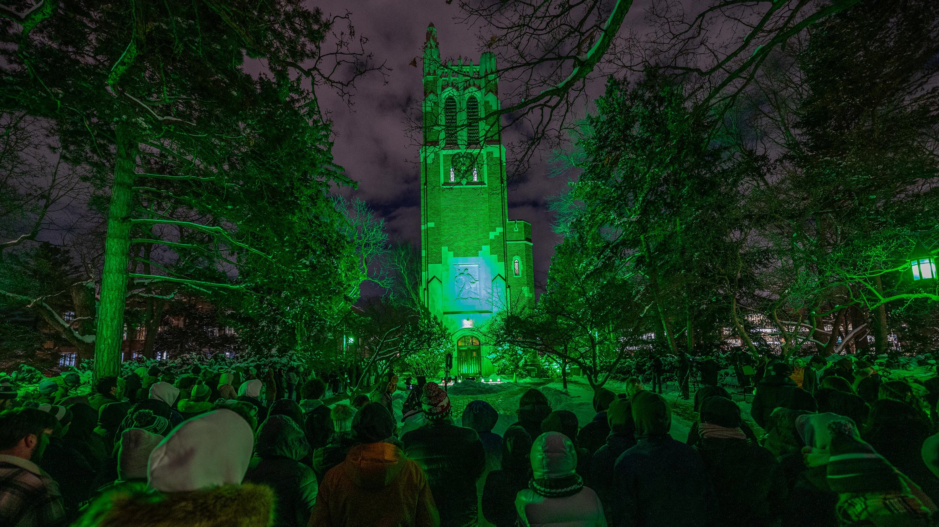 People standing in front of Beaumont Tower, which is illuminated by green light