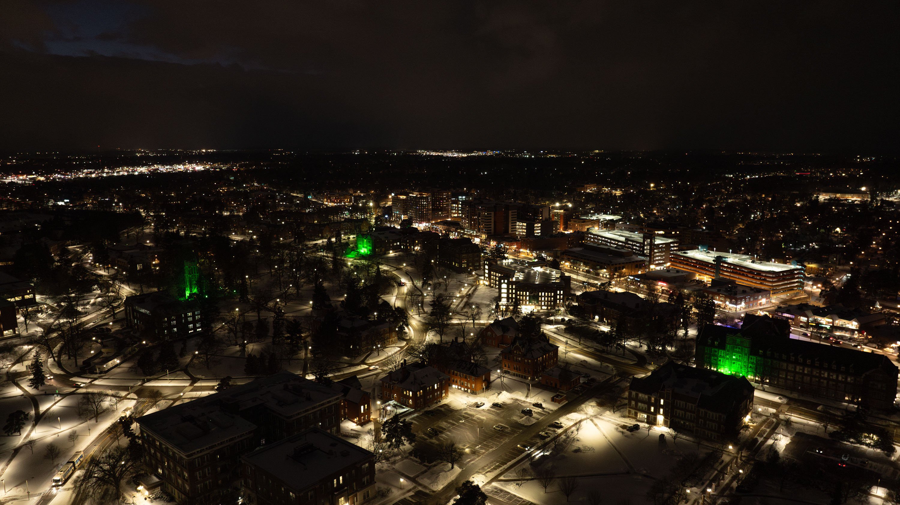 Overhead view of campus at night with the Union, Berkey Hall and Beaumont Tower lit with green light