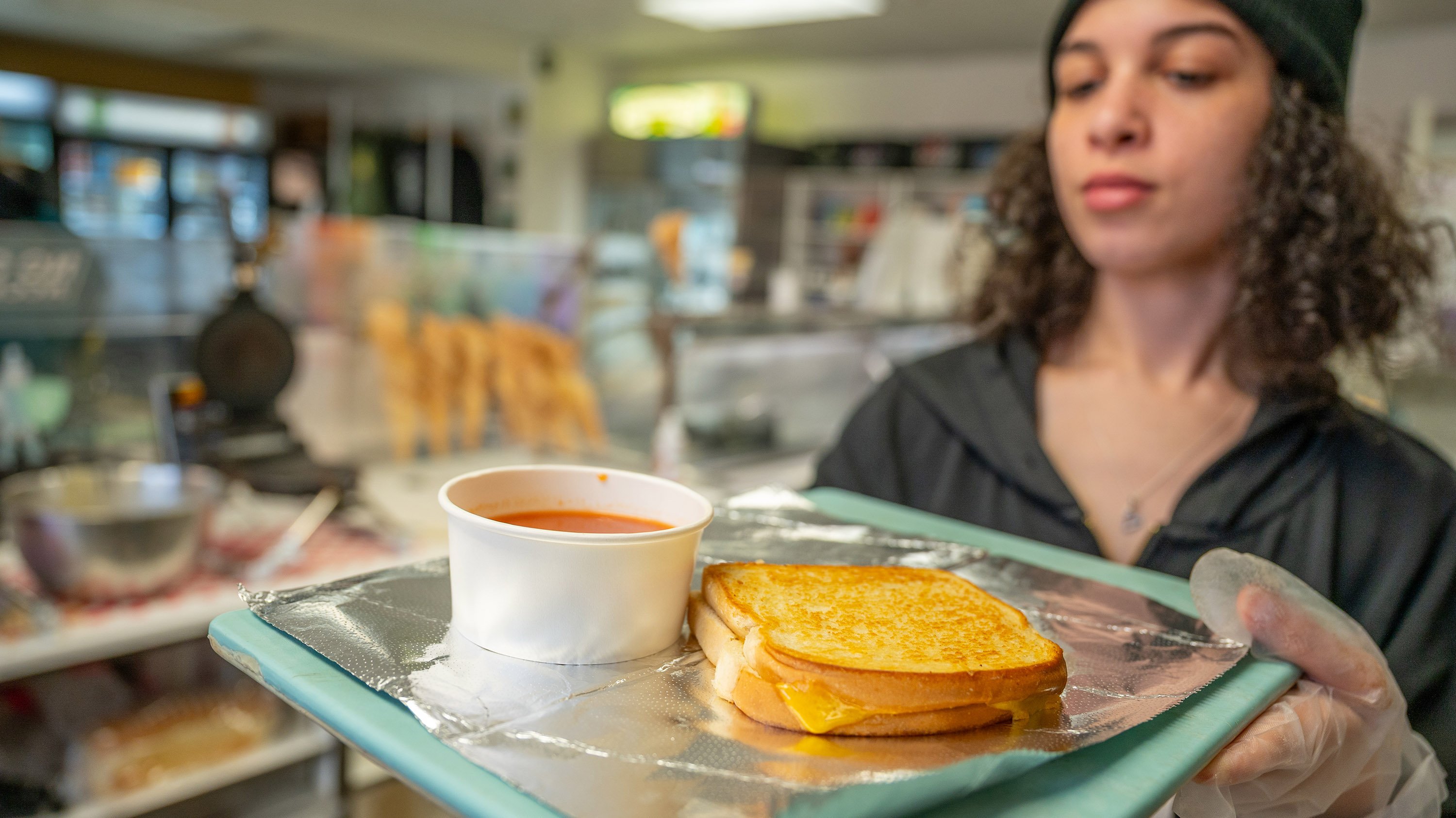 Student employee in MSU Dairy Store holding tray with grilled cheese and tomato soup