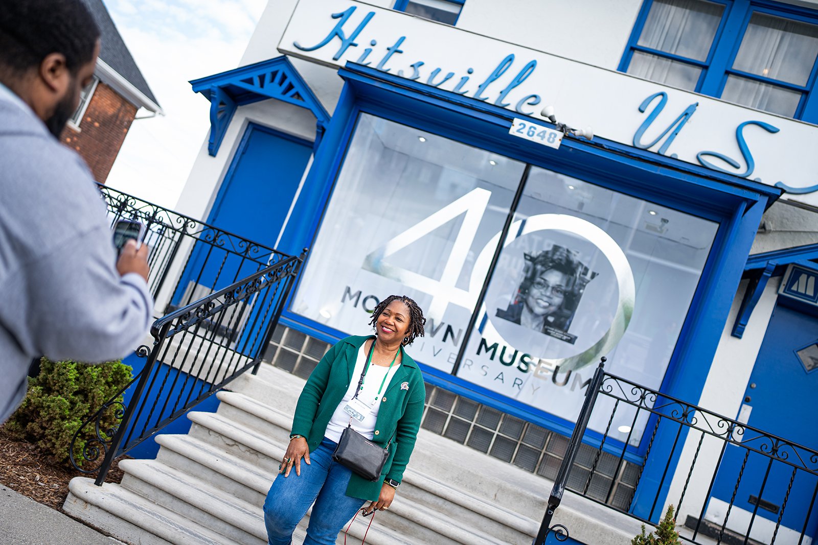A woman poses for a photo outside of a white building with royal blue doors and trim. The words ?Hitsville USA? are on the front of the building 
