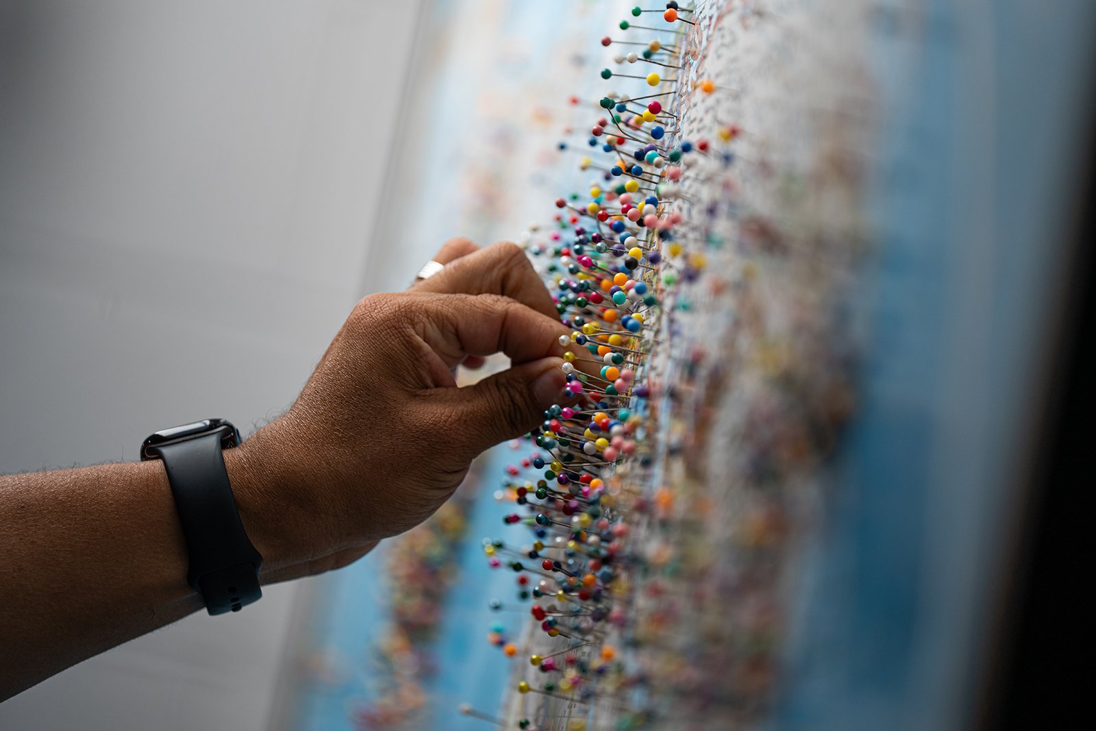 A hand puts a pin on a map. The map is covered in pins.
