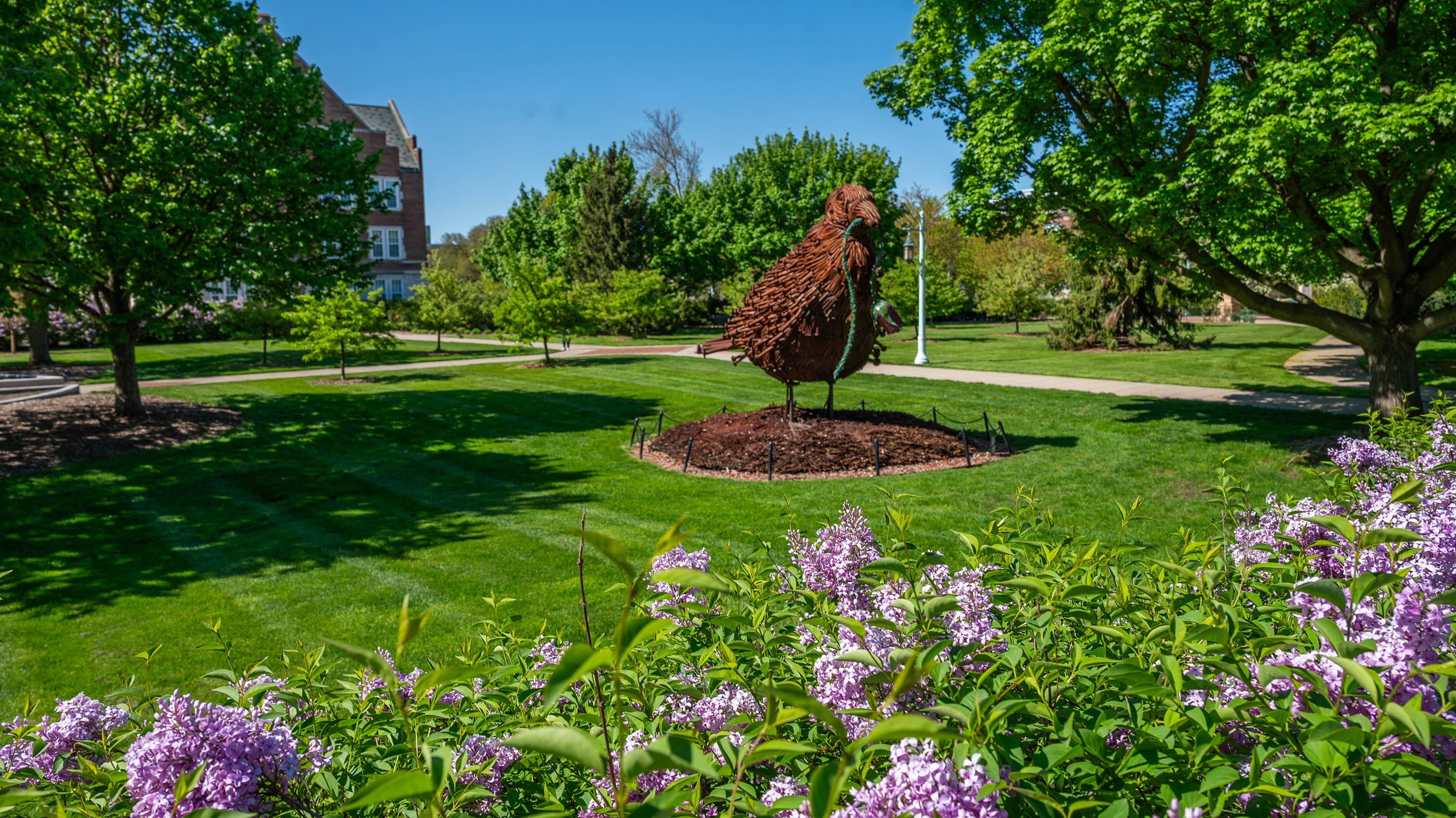 Bird sculpture behind lilac bushes